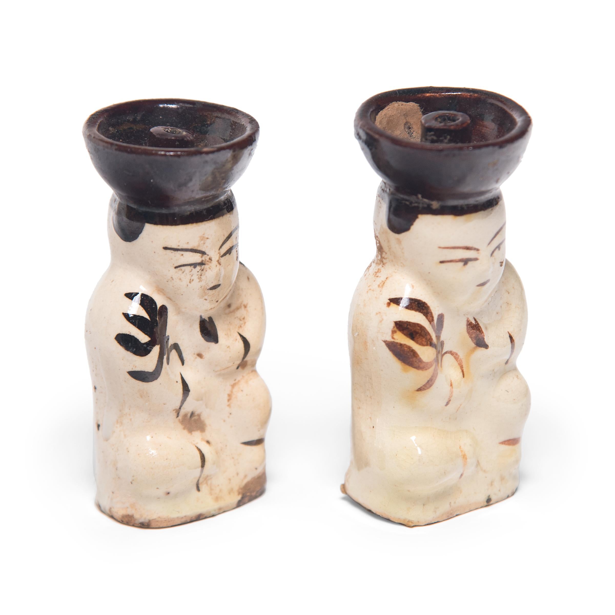 These early 20th century ceramic oil lamps are formed in the shape of a young boy, a motif often referred to as a 