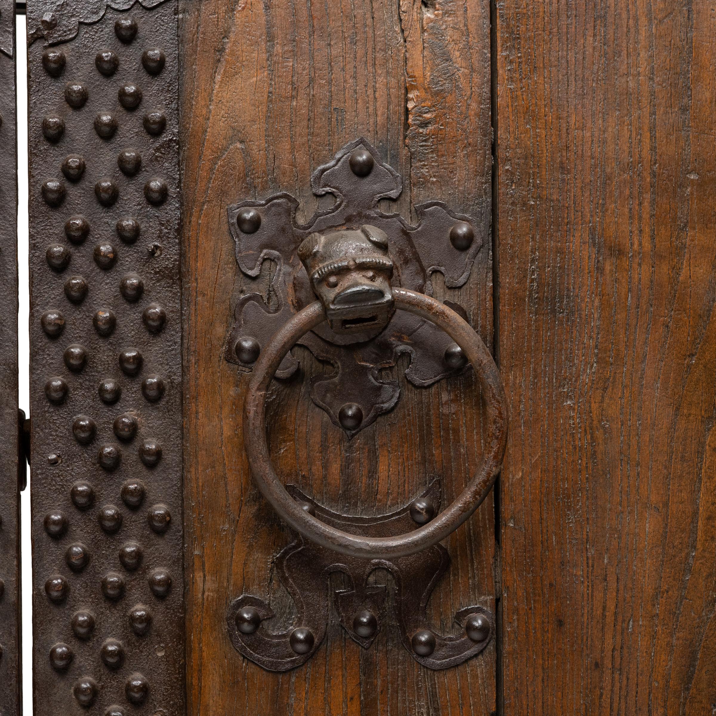 This impressive set of doors dates to the mid-19th century and originated as the outermost entrance gate to a traditional Qing dynasty courtyard home. Crafted of Northern elmwood (yumu) and hand-worked iron, this rustic door has developed a rich