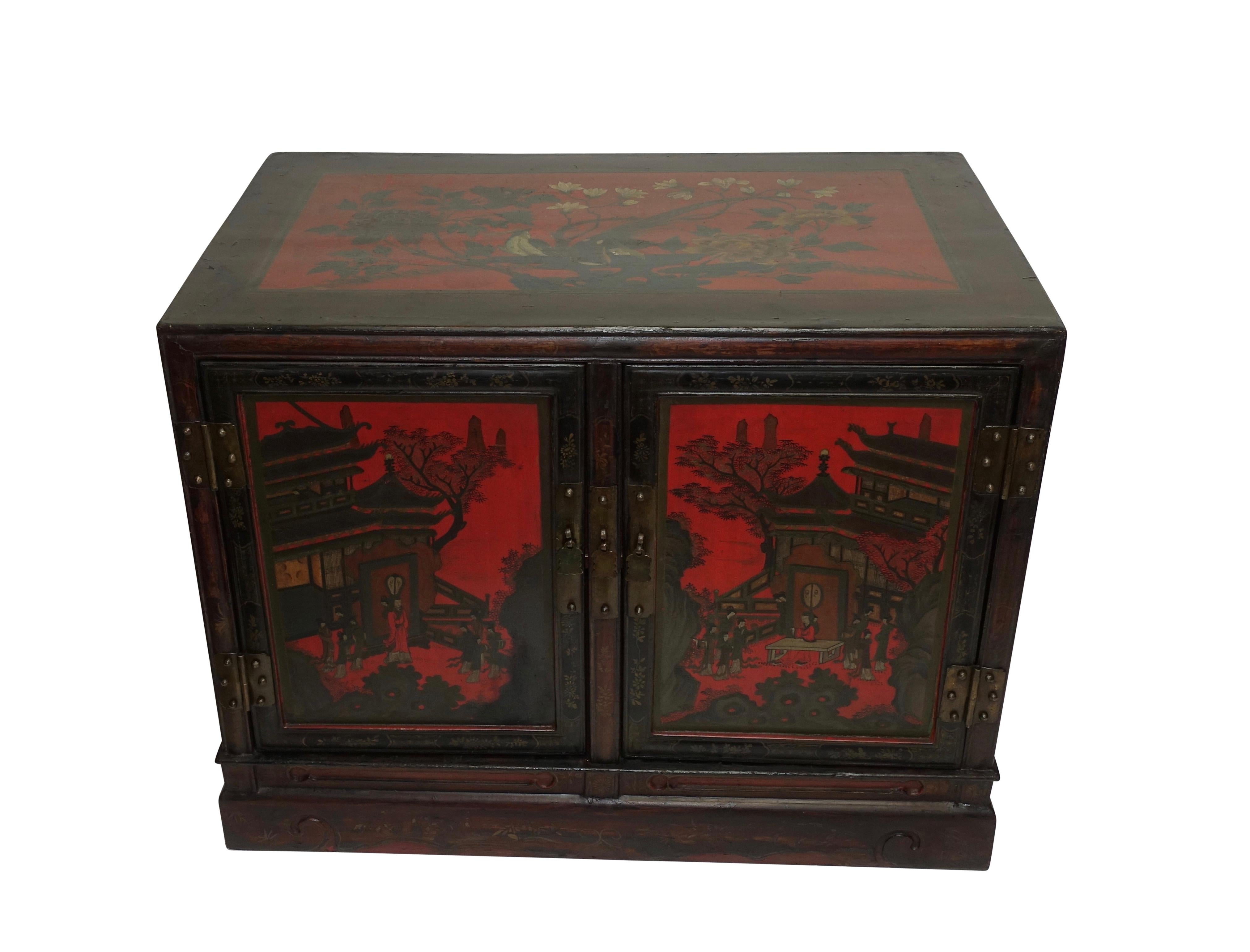 A pair of red and black lacquer ceremonial robe cabinets with a painted garden scene of figures and flowers, having brass hardware and handles. The back side has been lacquered and painted as well. China, Qing dynasty, mid-19th century.