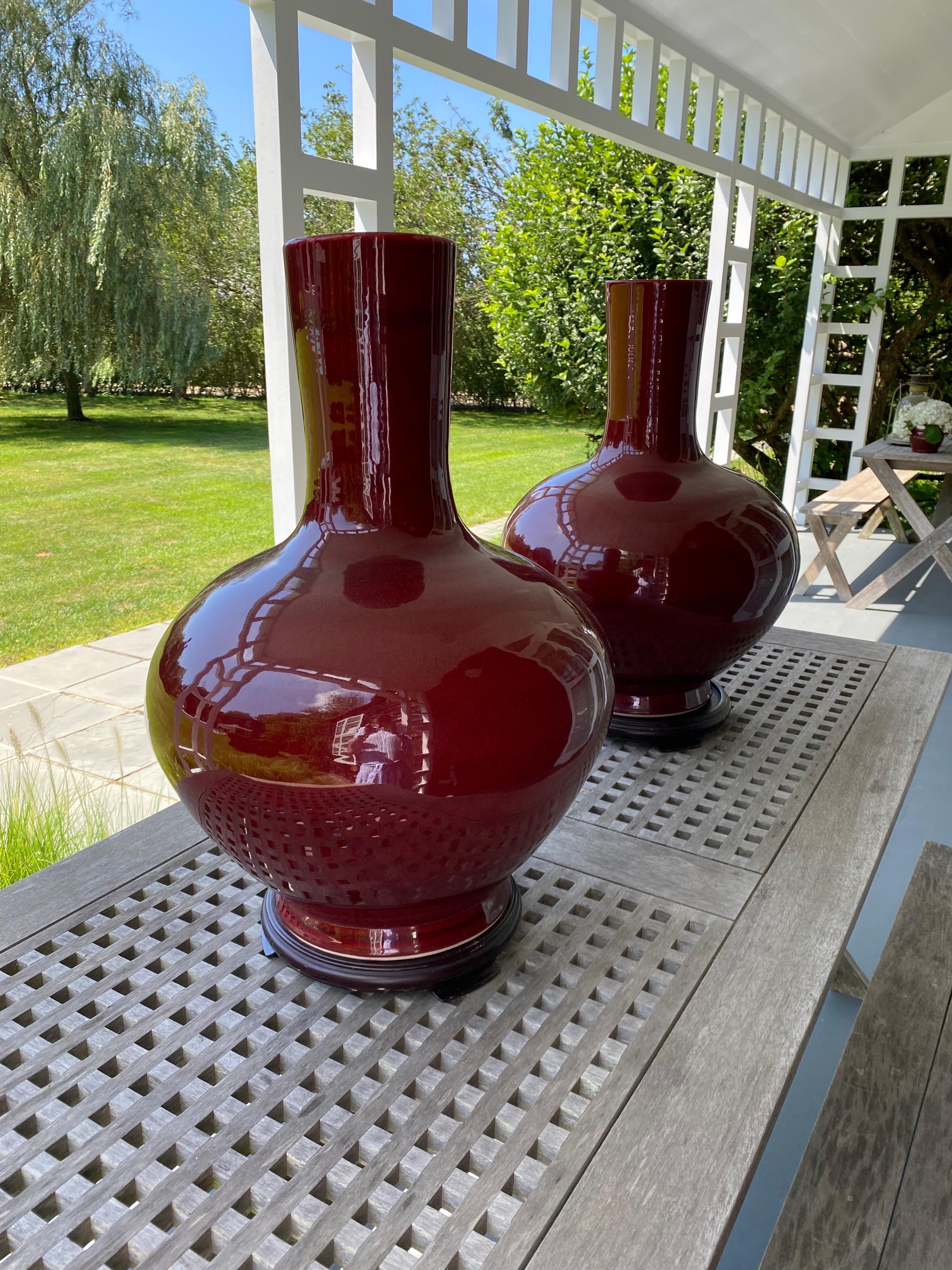 Pair of Chinese Large Sang-de-Boeuf glazed red vases, early 20th century on Wood Plinths. Round bulbous form with an elegant clean neck sat on a wooden plinths and glazed in deep red glaze. Also called flambé glaze, a glossy, rich, blood red glaze