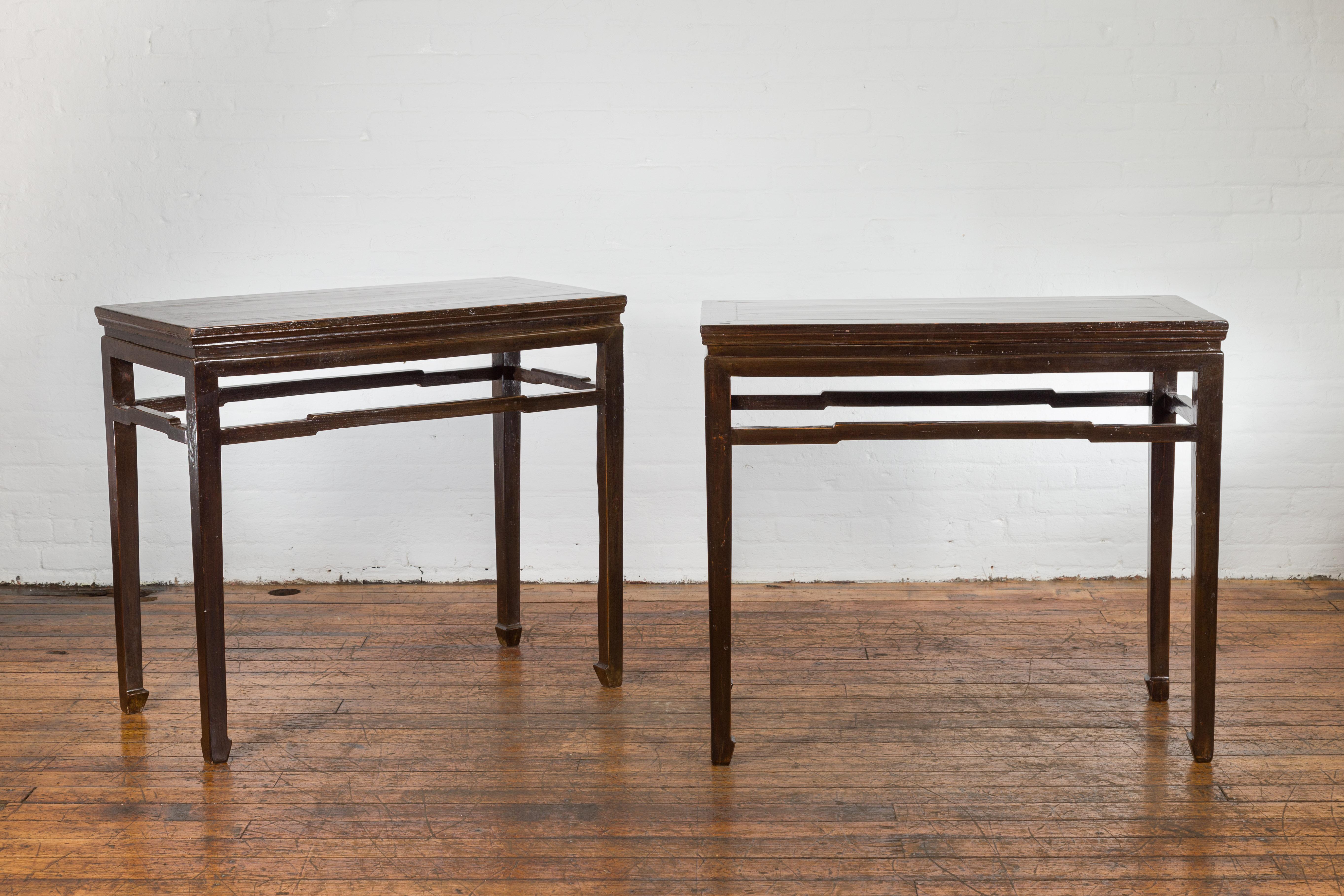 A pair of Chinese late Qing Dynasty period wine tasting console tables from the early 20th century, with humpback stretchers, horse hoof feet and dark brown lacquer. Created in China during the late Qing Dynasty period in the early years of the 20th