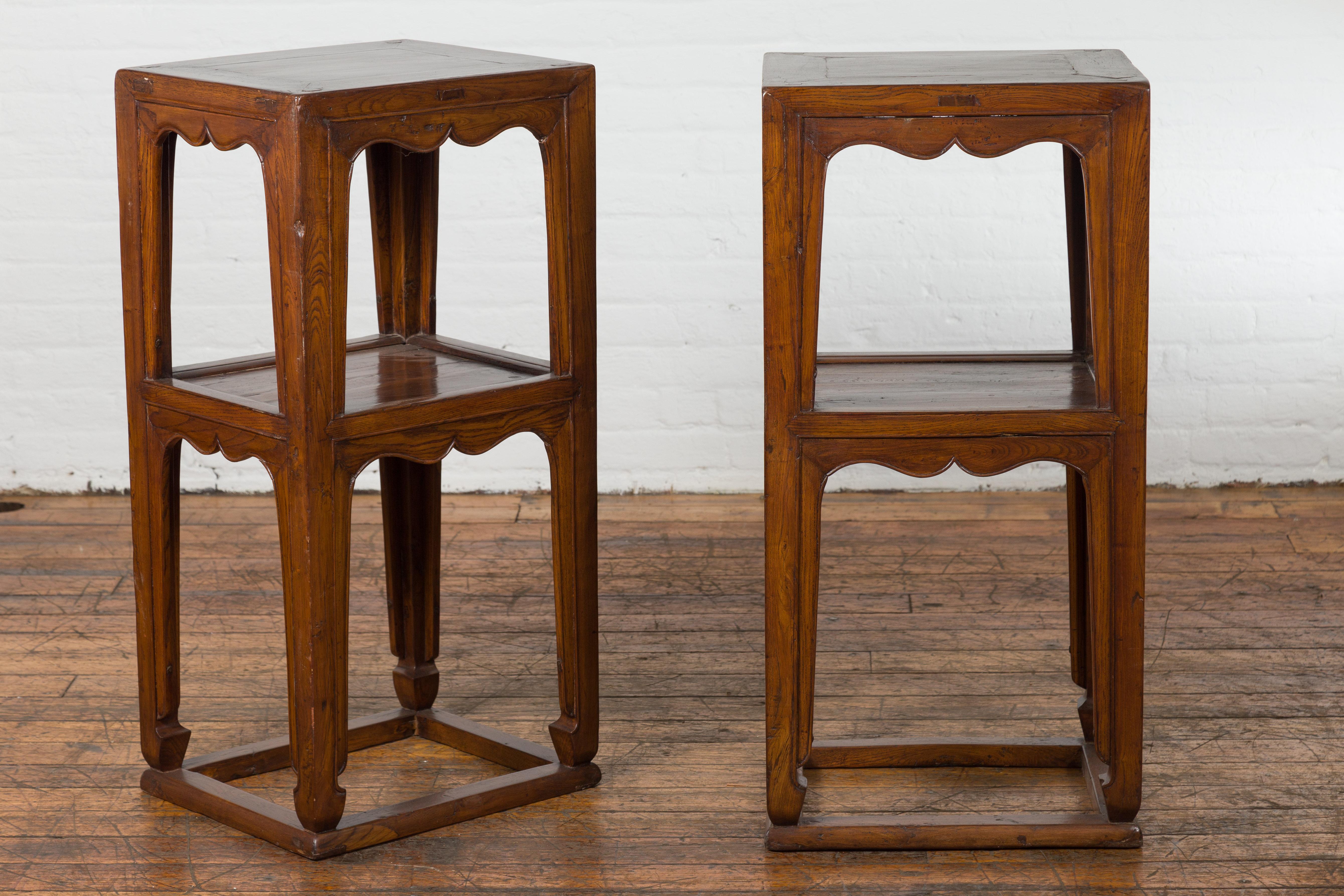 A pair of late Qing Dynasty period tiered lamp tables from the early 20th century, with carved aprons, shelves, horse hoof feet and low stretchers. Created in China during the late Qing Dynasty period in the early years of the 20th century, this