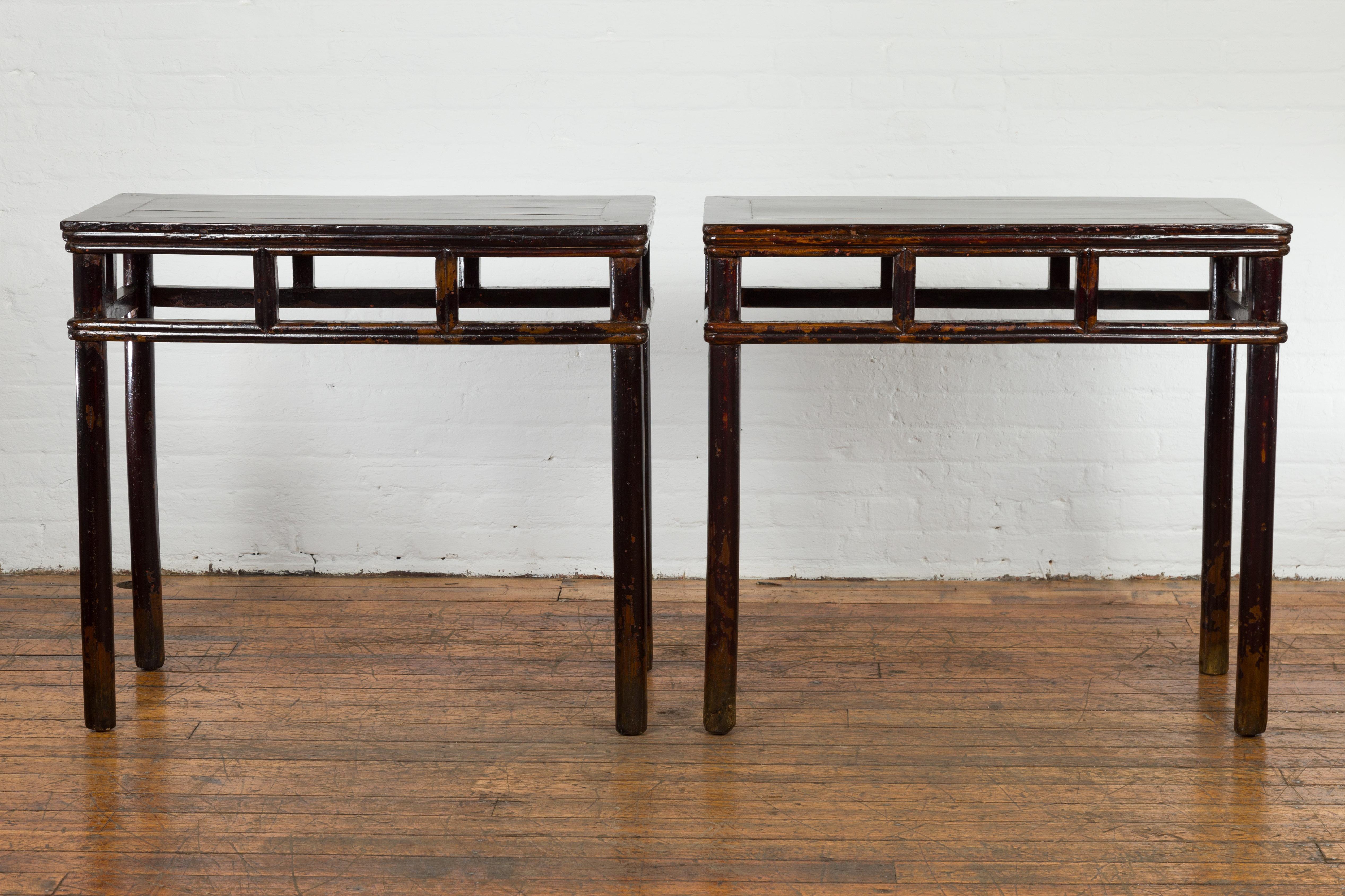 A pair of Chinese late Qing Dynasty period wine console tables from circa 1900 with black/brown lacquer, open apron, pillar strut motifs and distressed patina. Presenting an exquisite pair of Chinese wine console tables from the late Qing Dynasty