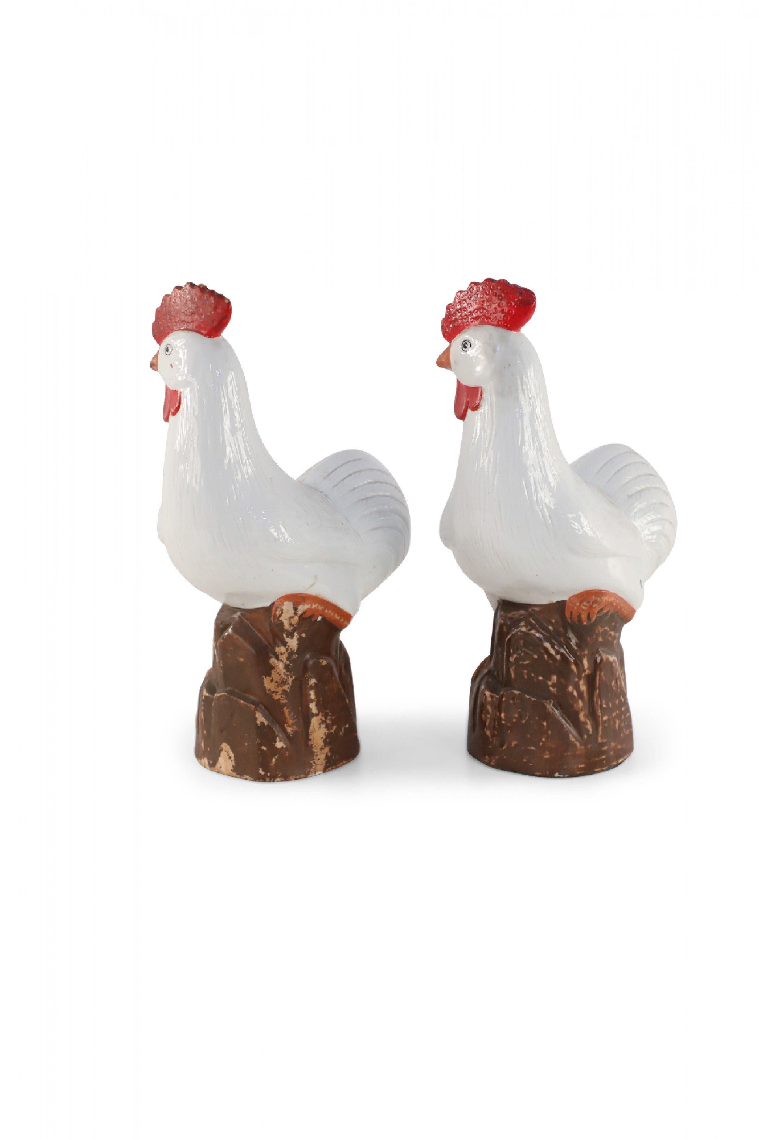 Pair of antique Chinese (mid 20th century) white porcelain chickens, detailed with tonal feathers and red features and sculpted perched on rocks (priced as pair).
  