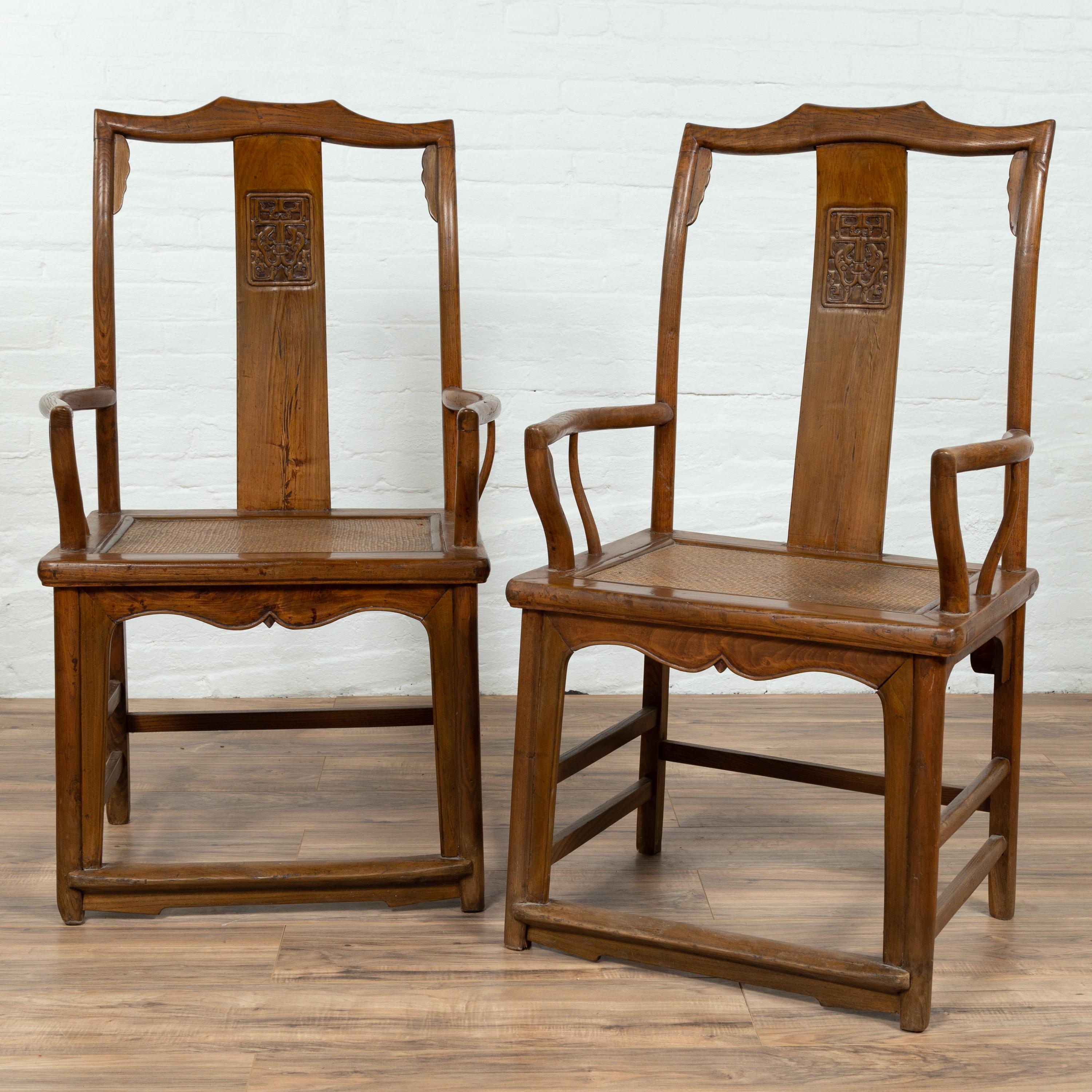 A pair of Chinese Ming Dynasty style elm scholar's chairs from the early 20th century, with unusual upper rail, carved panels on the splats, curved arms and rattan seats. Born in China during the early years of the 20th century, each of this pair of