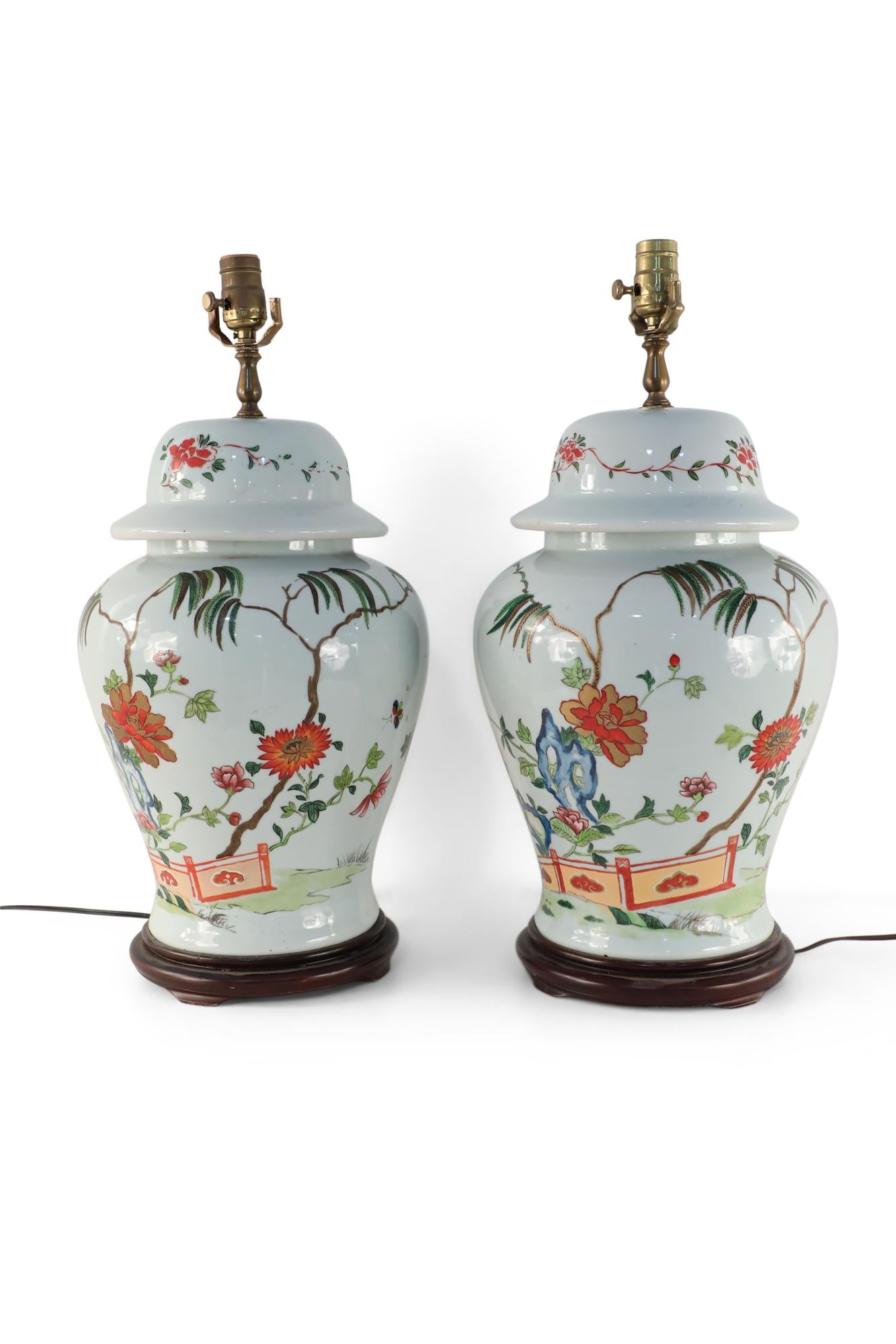 Pair of Chinese porcelain table lamp urn-shaped vases decorated with a pastoral scene of flowers and bamboo growing from behind a decorative gate mounted on wooden bases with brass hardware.