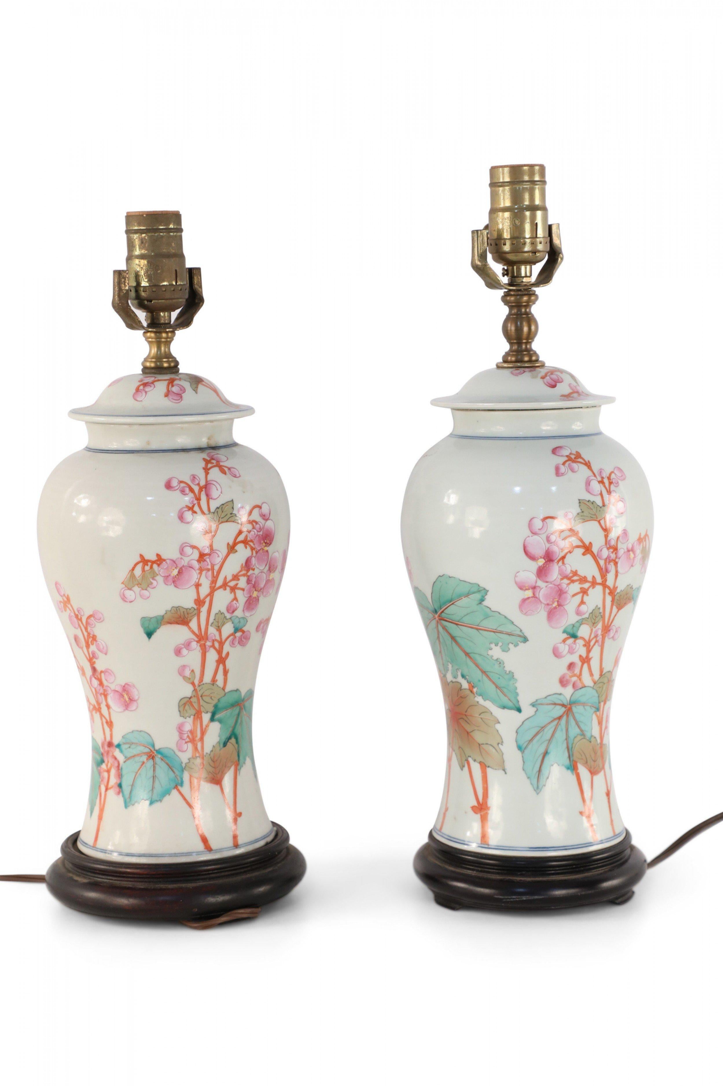 Pair of similar Chinese porcelain table lamps made from off-white, urn-shaped vases with pink, orange and green florals, berries, leaves and snap dragons with wooden bases and brass hardware (lamps vary slightly in height and pattern) (PRICED AS