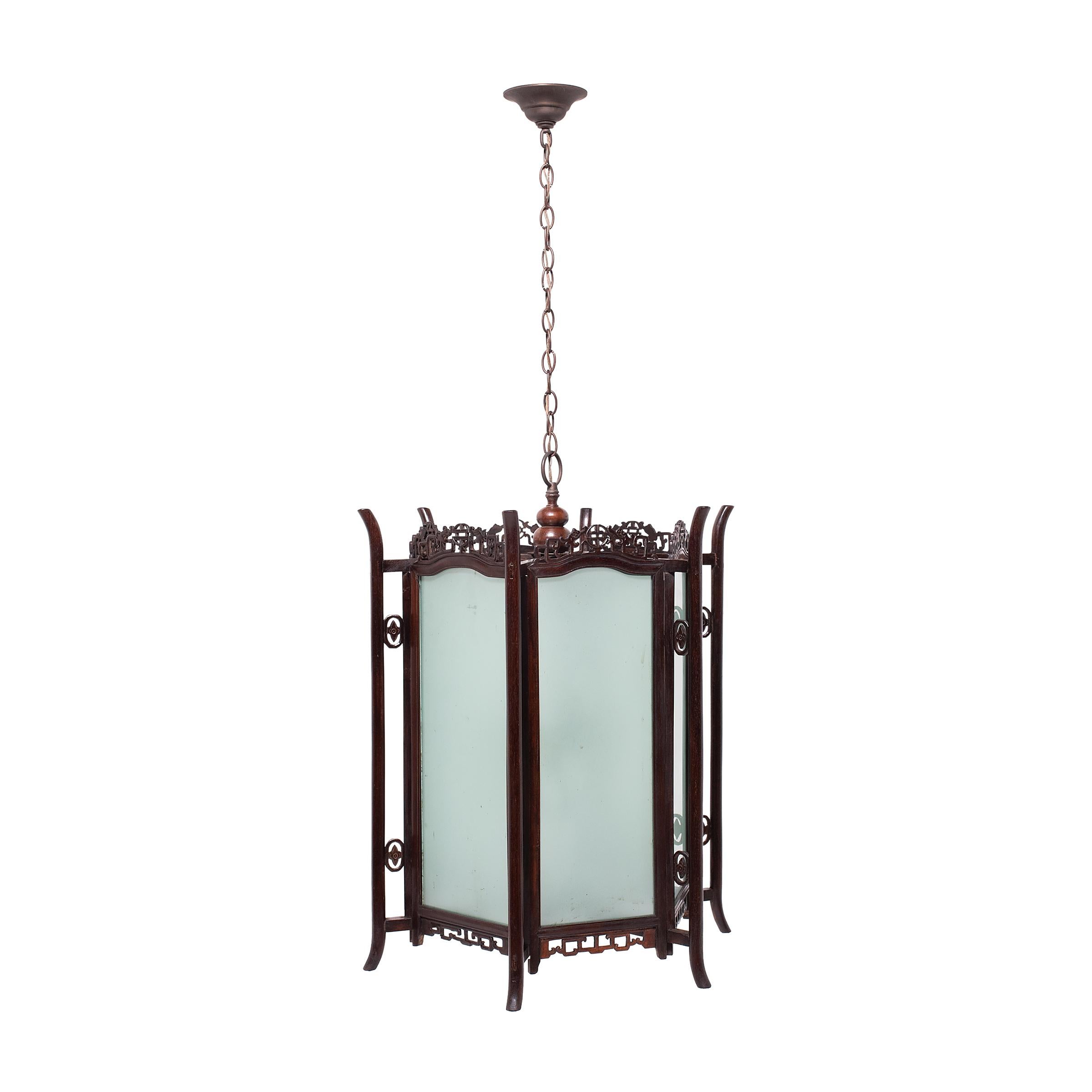 Expertly constructed with beautiful rosewood frames and frosted glass panels, these ornate hanging lanterns once diffused candlelight throughout a fine Qing-dynasty courtyard home. Each lantern has a hexagonal design, with six elongated glass panels