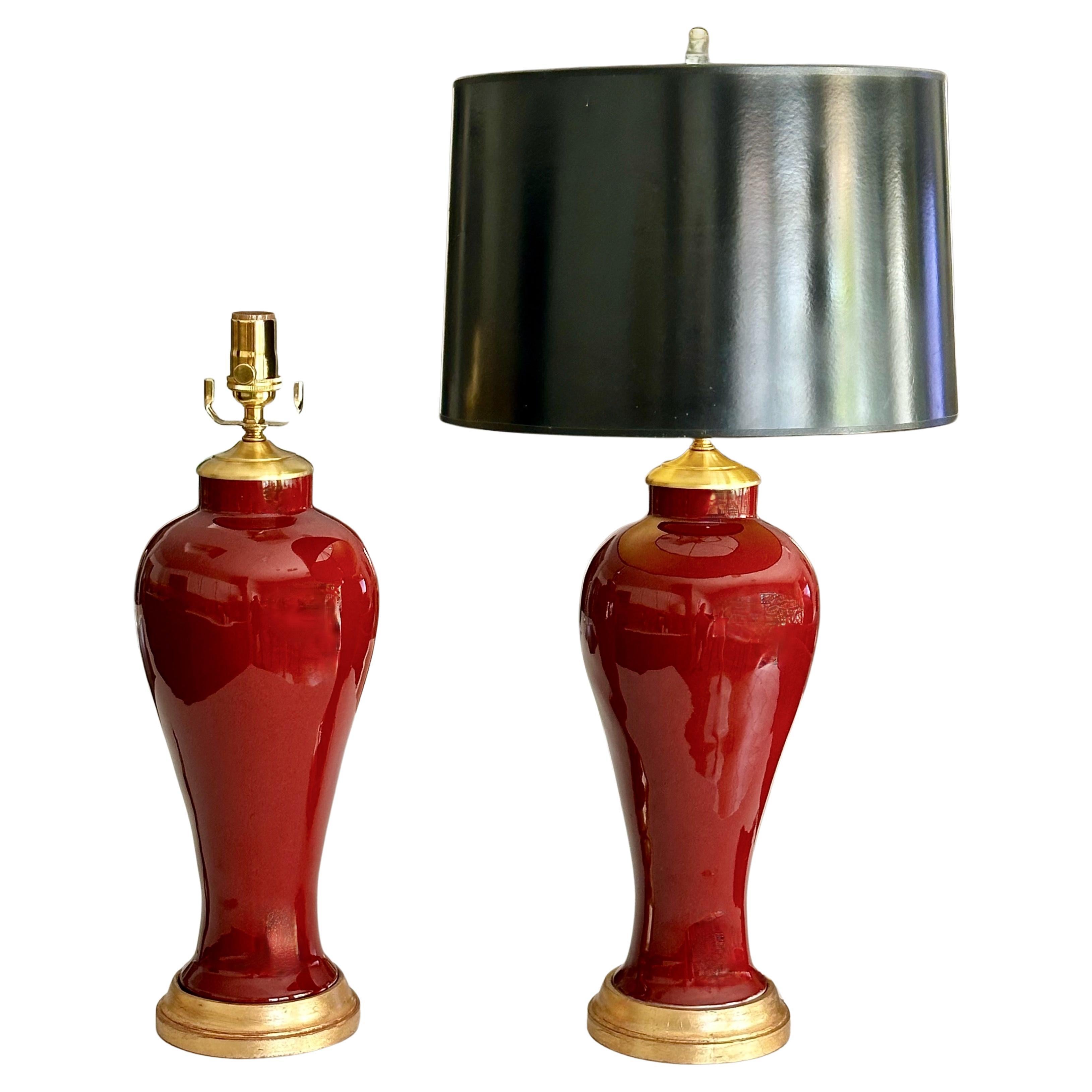Paar chinesische Vasen aus ochsenblutfarbenem Porzellan auf vergoldeten Lampenfüßen aus Holz. Ergänzt mit Messingbeschlägen. Neu verkabelt mit neuen 3-fach Steckdosen und braunen Corden. Gesamthöhe oberhalb des Sockels 20,5