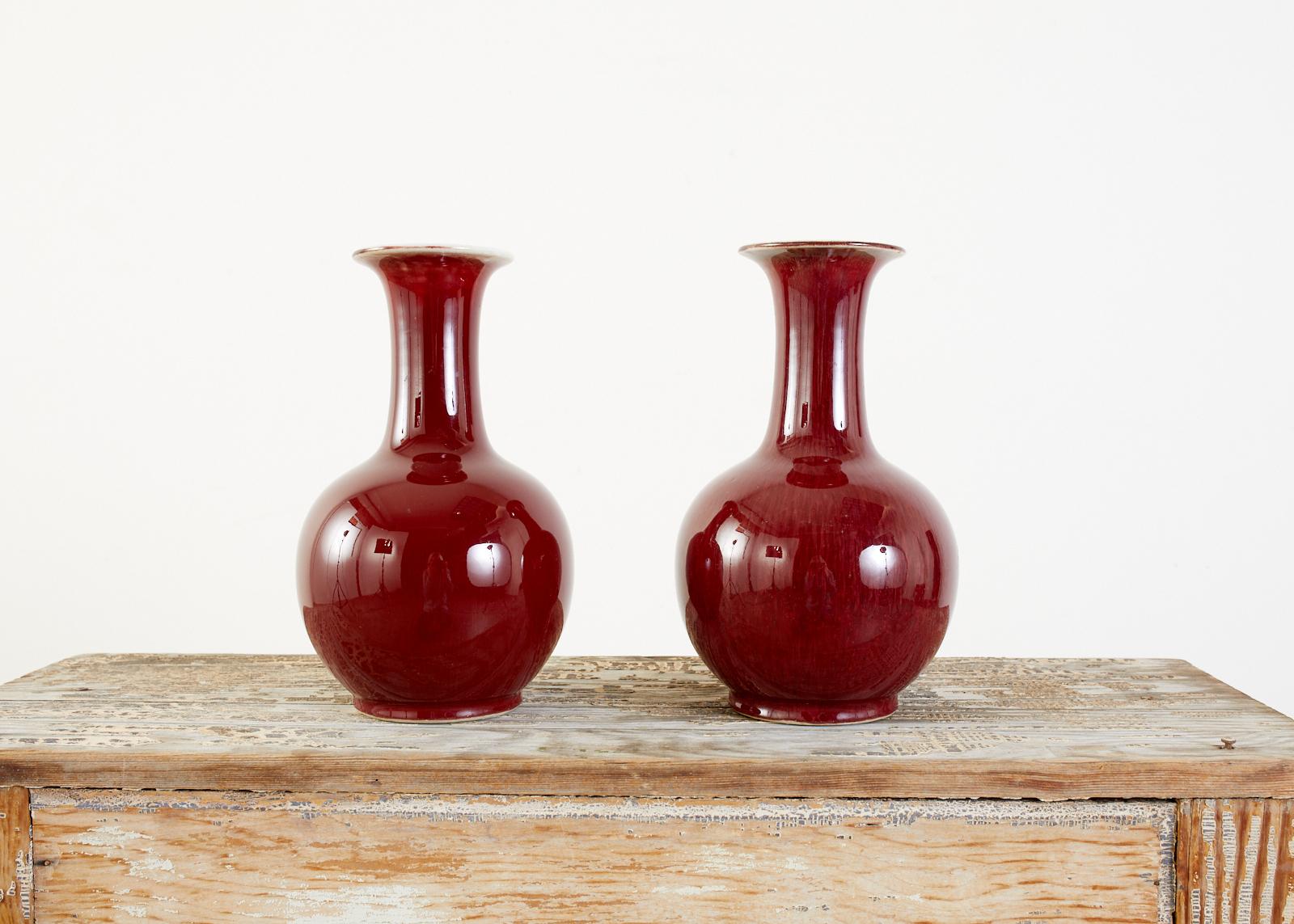 Distinctive pair of Chinese export vases featuring a deep oxblood Sang de Boeuf color on the Langyao glaze. The vases have a long waisted neck and globular belly. Made in the Jingdezhen kilns the vases have a very fine craquelure on the finish. One
