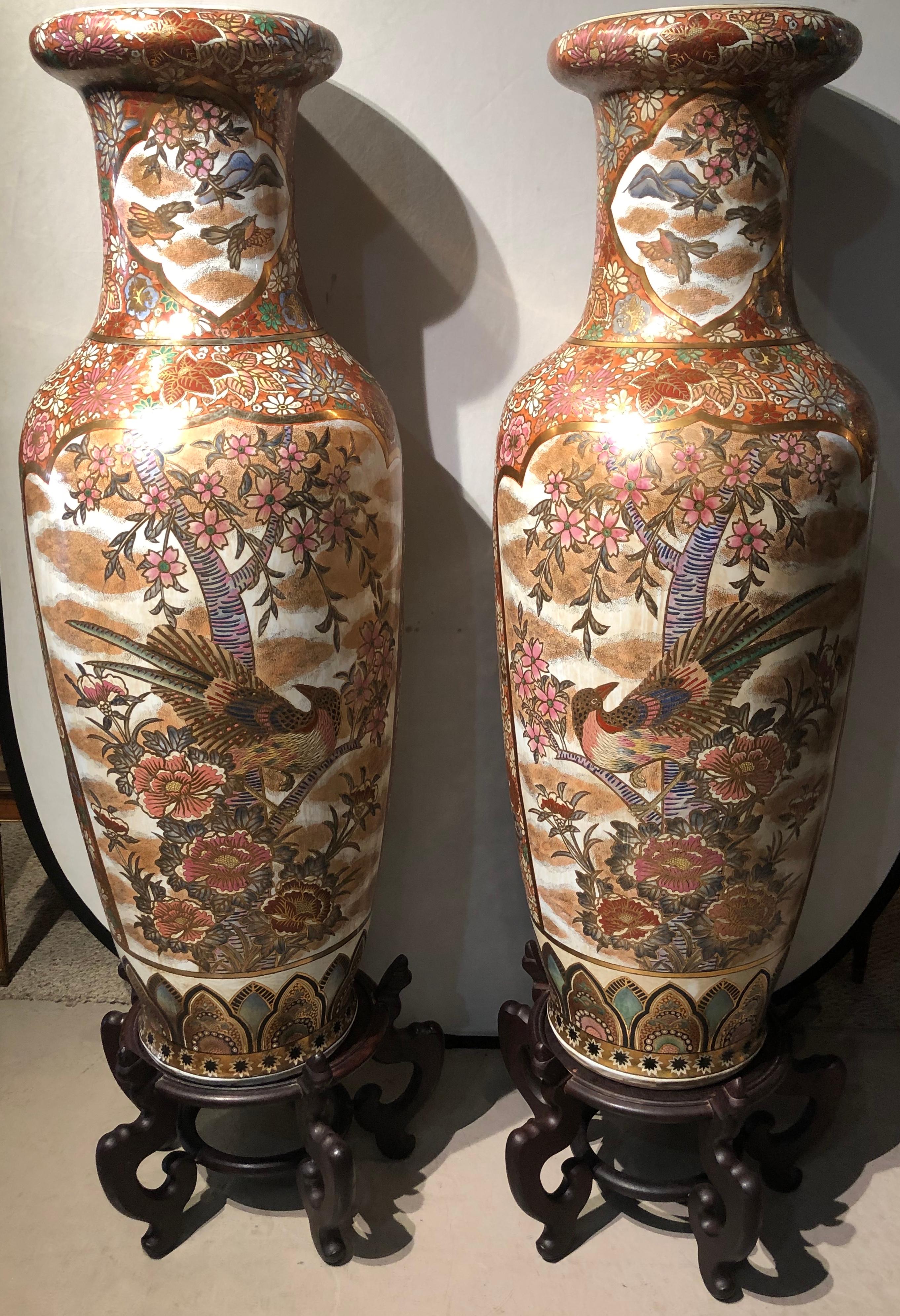 Pair of Chinese Palatial vases or urns on sleek and simple teak pedestals each having opposing bird decorations with fine gilt and floral design. Each with a signed base.