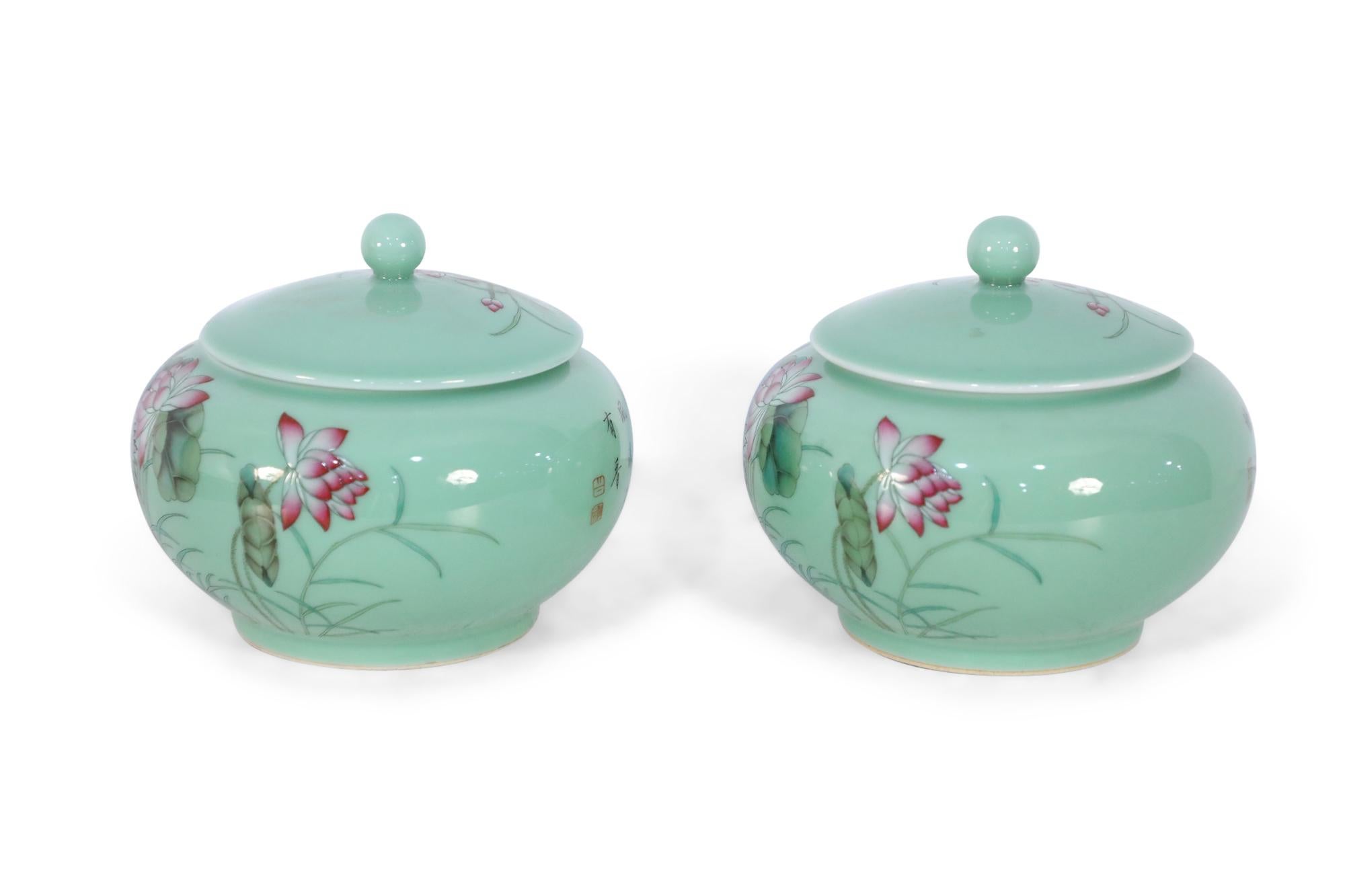 Pair of Chinese pale green lidded jars decorated with lily pads and pink lotus blossoms on one side of their round forms and extending up to the lids, and characters on the reverse sides (date mark on bottom, see photos).