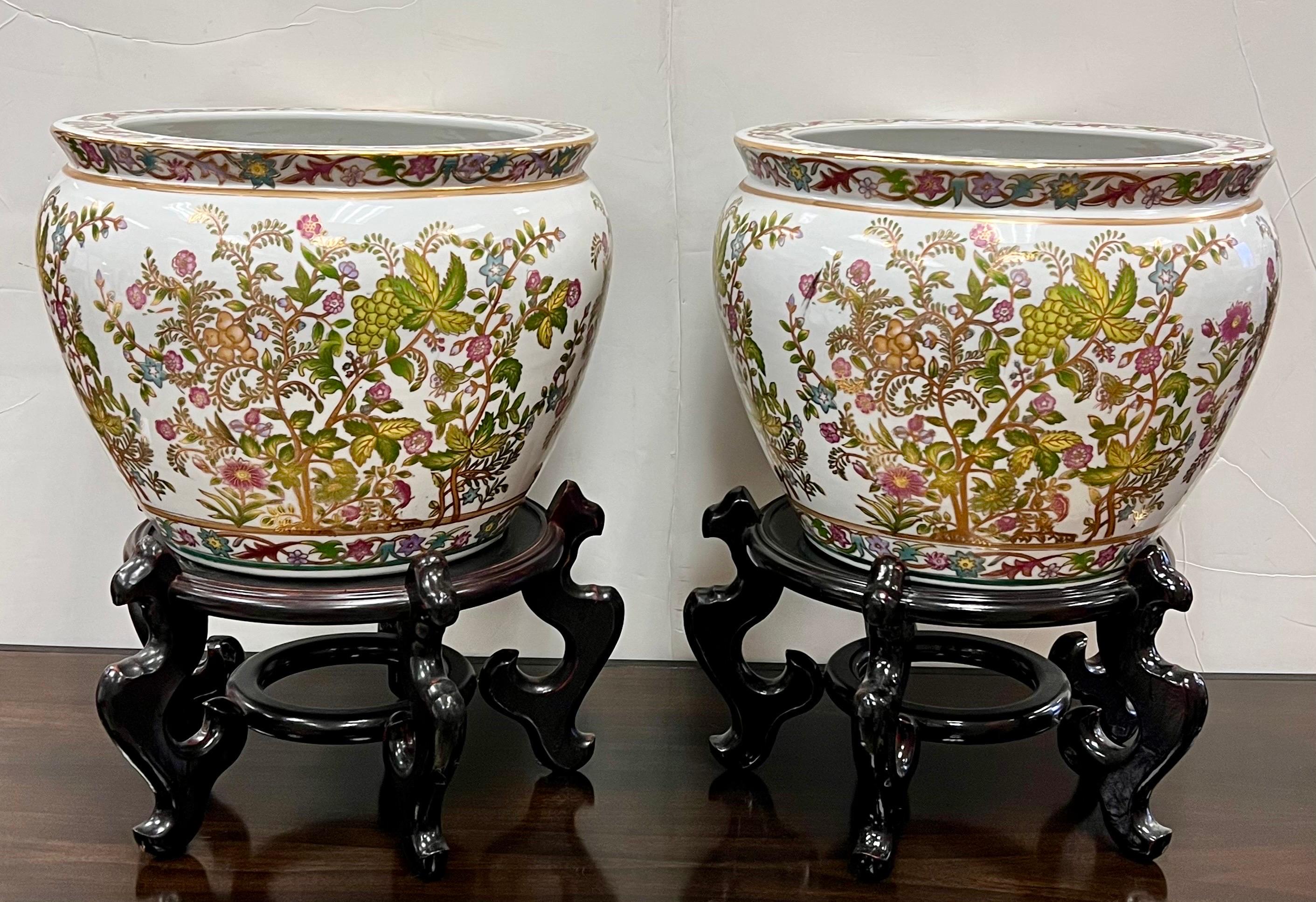 Magnificent pair of Chinese porcelain jardinieres fishbowls planters in a pink and green floral motif.  On carved wooden pedestal bases.