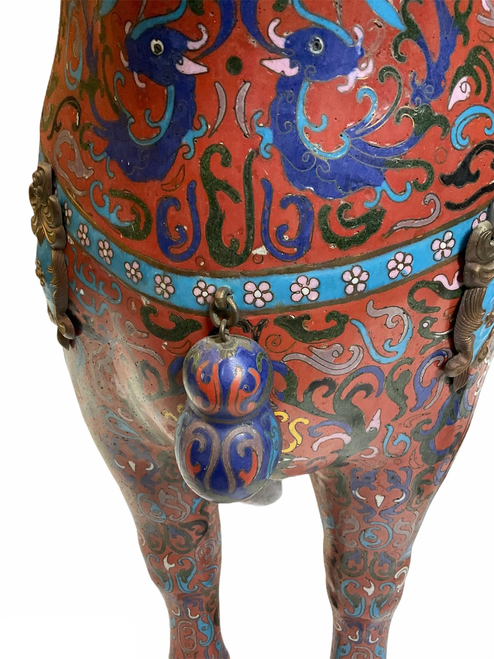 This is a pair of Chinese enamel cloisonné brass standing up horses. Their background is red wine color decorated with a mix of polychromatic scrolls, shields, seahorses and dragons. They are also embellished with a turquoise belts with flowers that