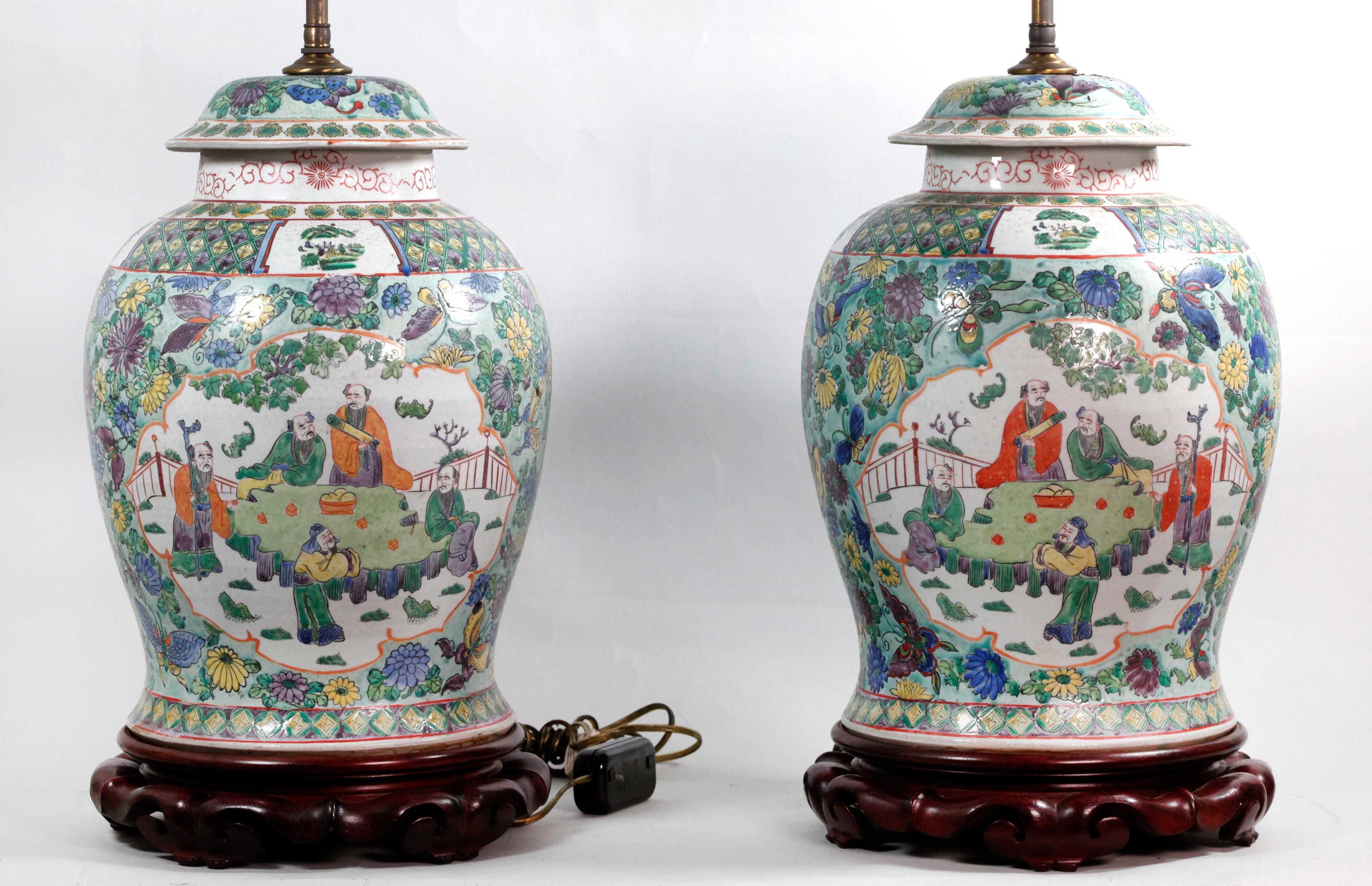 les pots de couverture ont été transformés en lampes ; décorés de scènes figuratives sur un motif floral, fond vert ; mesures approximatives de chaque pot de couverture avec la base en bois : 18po(H) x 9.5po(diamètre) ; mesures approximatives de
