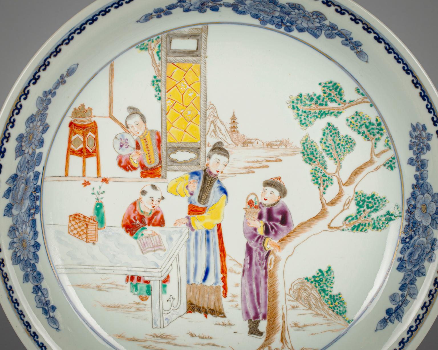 With figures in an outdoor setting, the wide everted border painted in underglaze blue with flowers and light gilding.