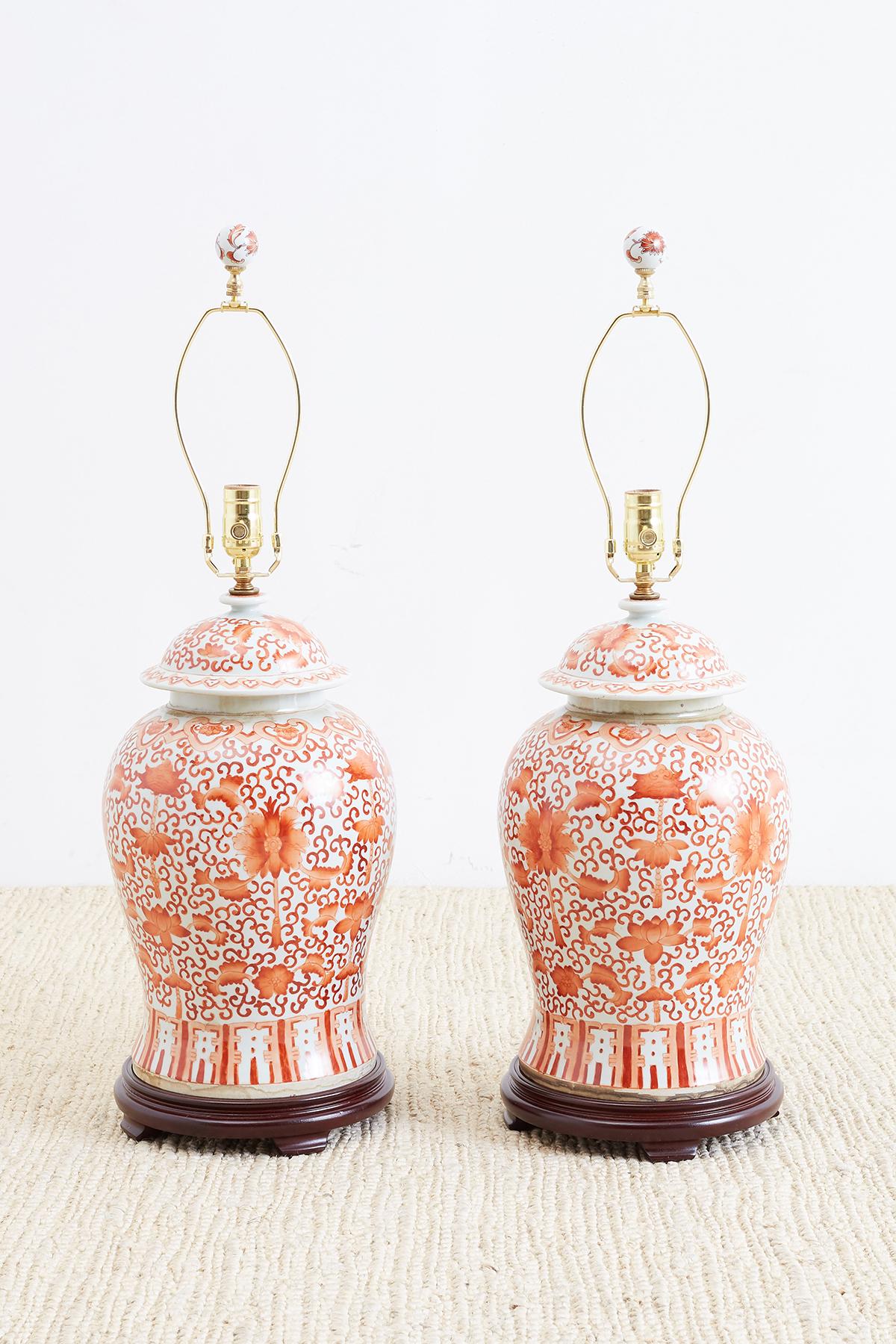 Exceptional pair of large Chinese porcelain hand-painted ginger jar table lamps. Featuring lidded jars decorated with lotus blossom and peonies. The background is a scrolling vine pattern and the flowers have a faded brick color. Rewired with new