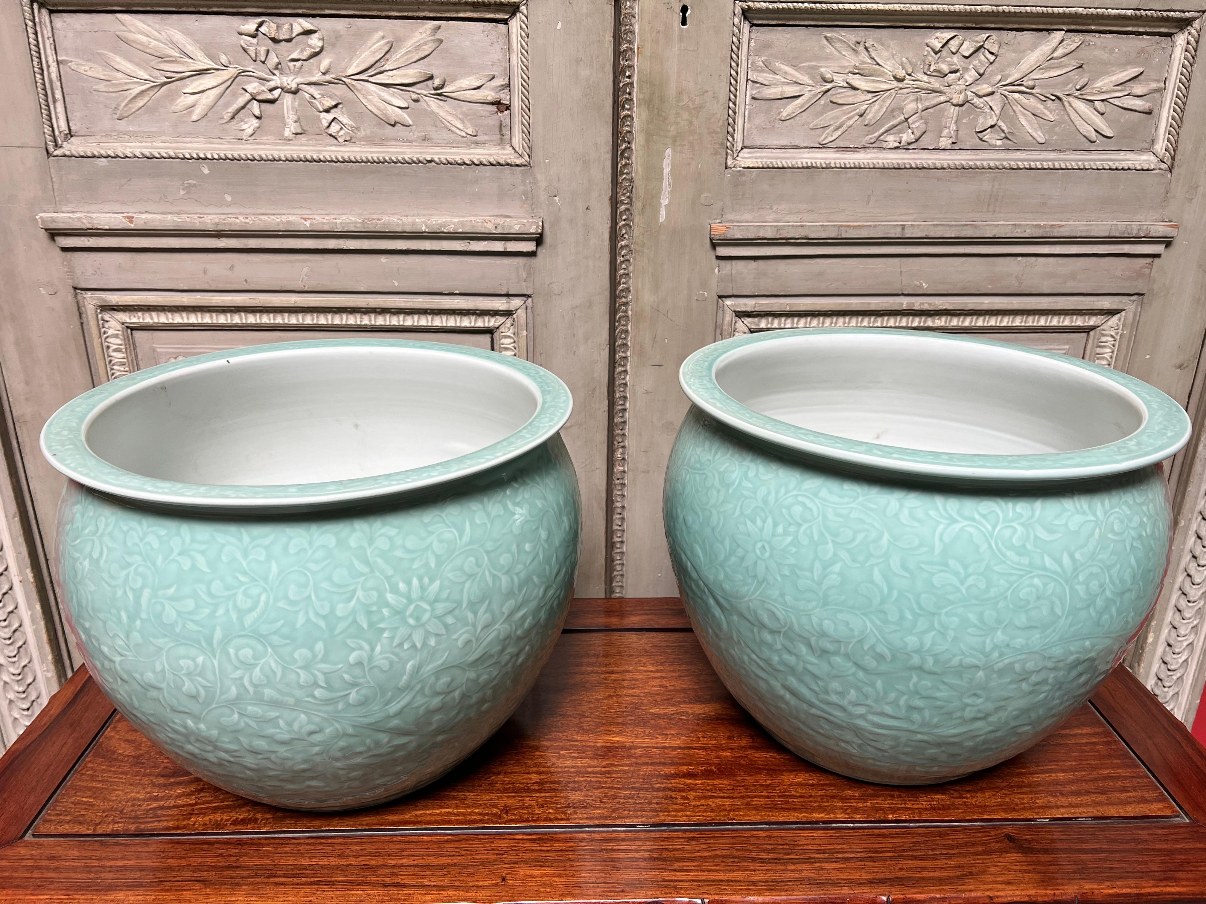 A pair of Chinese porcelain fish bowls with a celadon glaze and embosed floral design. These jardinieres are a nice scale with a beauiful colored glaze. They are in good condition and are very good reproductions of high quality from the 1980s.