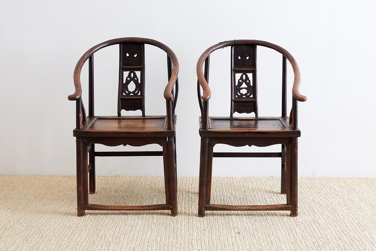Beautifully worn pair of Chinese Qing dynasty provincial horseshoe armchairs. Constructed from elm with a rich patina and interesting old repairs made with pieces of iron. Both chairs have a pierced back splat with scrolled designs and a shaped seat
