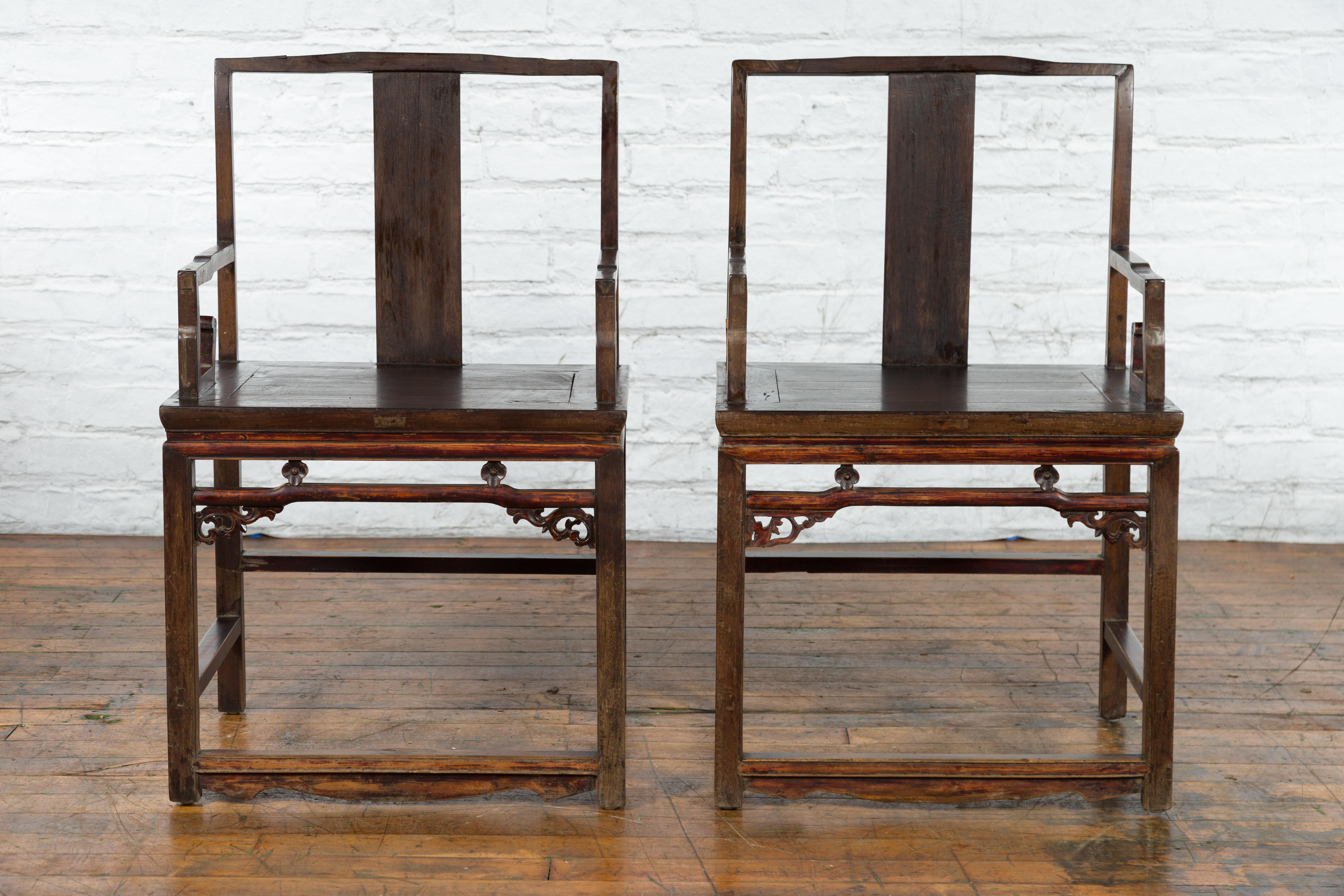A pair of Chinese Qing Dynasty period armchairs from the 19th century, with open backs, scrolling arms, carved aprons and low stretchers. Created in China during the Qing Dynasty period in the 19th century, each of this pair of armchairs features an