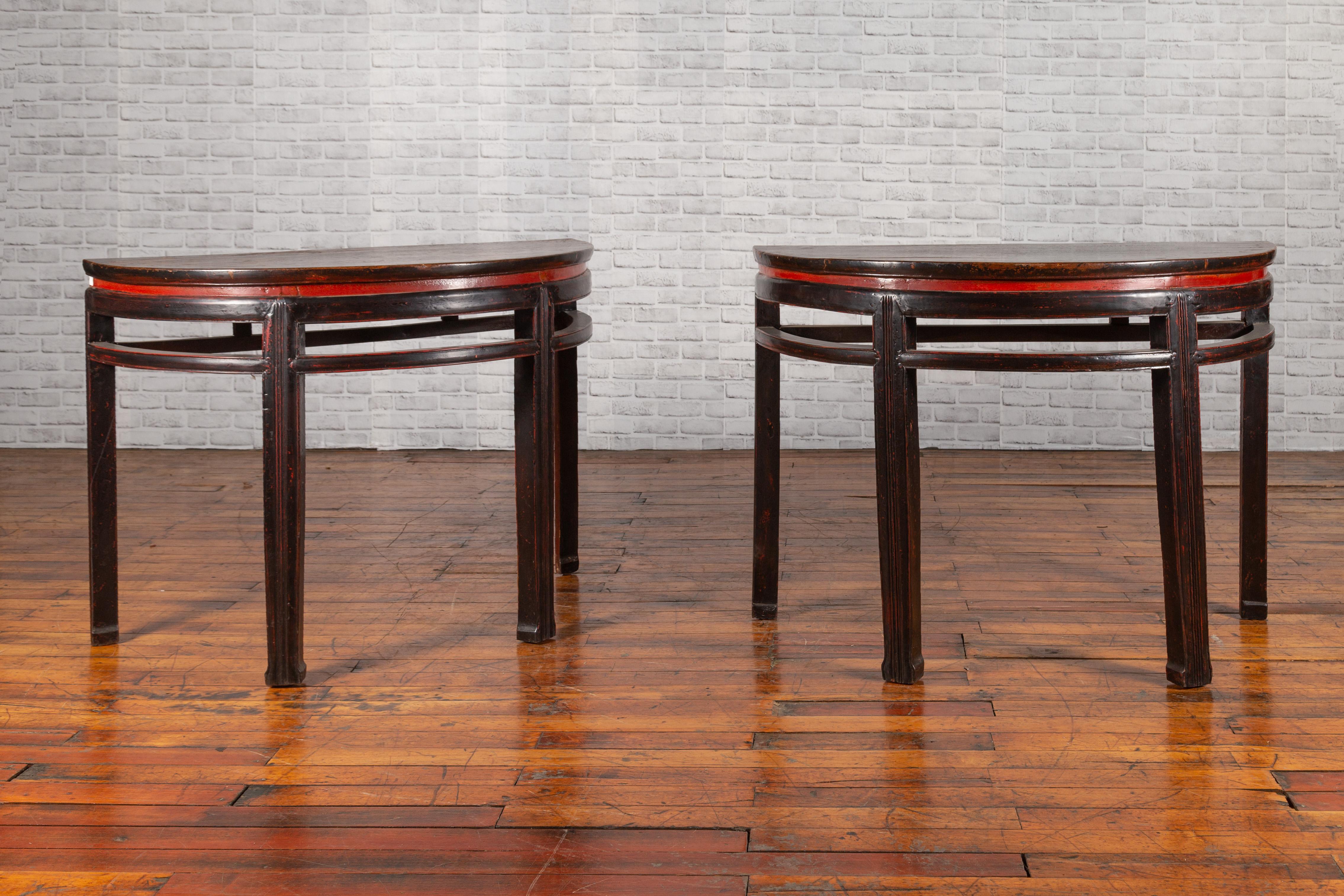 A pair of Chinese Qing Dynasty period demilune console tables from the 19th century, with original black and red lacquer. Created in China during the Qing Dynasty, each of this pair of demilunes features a semi-circular top showcasing a nicely