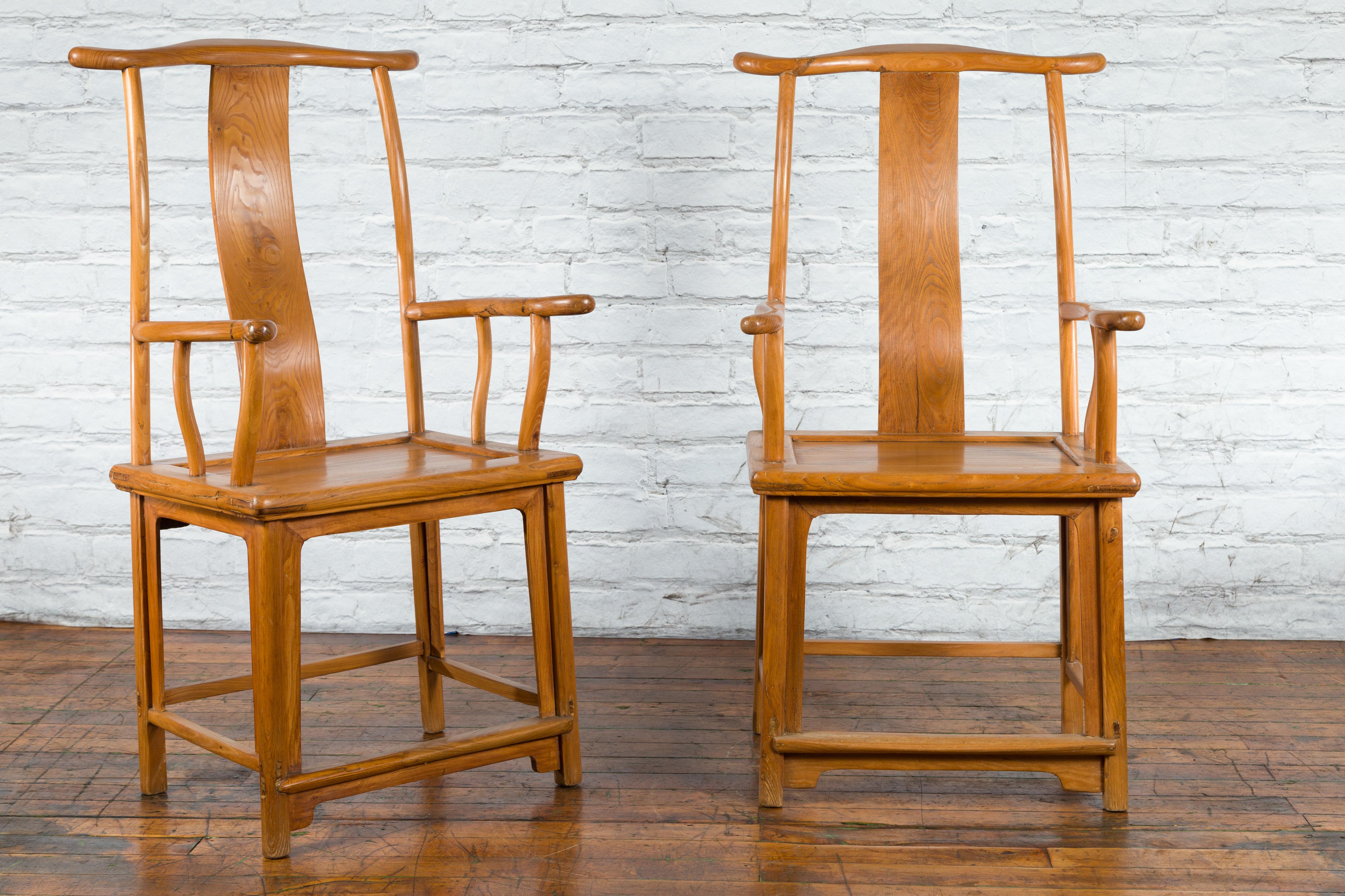 A pair of Chinese Qing Dynasty period lamp hanger armchairs from the 19th century with serpentine arms, wooden seats and natural honey patina. Created in China during the Qing Dynasty period, each of this pair of armchairs features a rectangular
