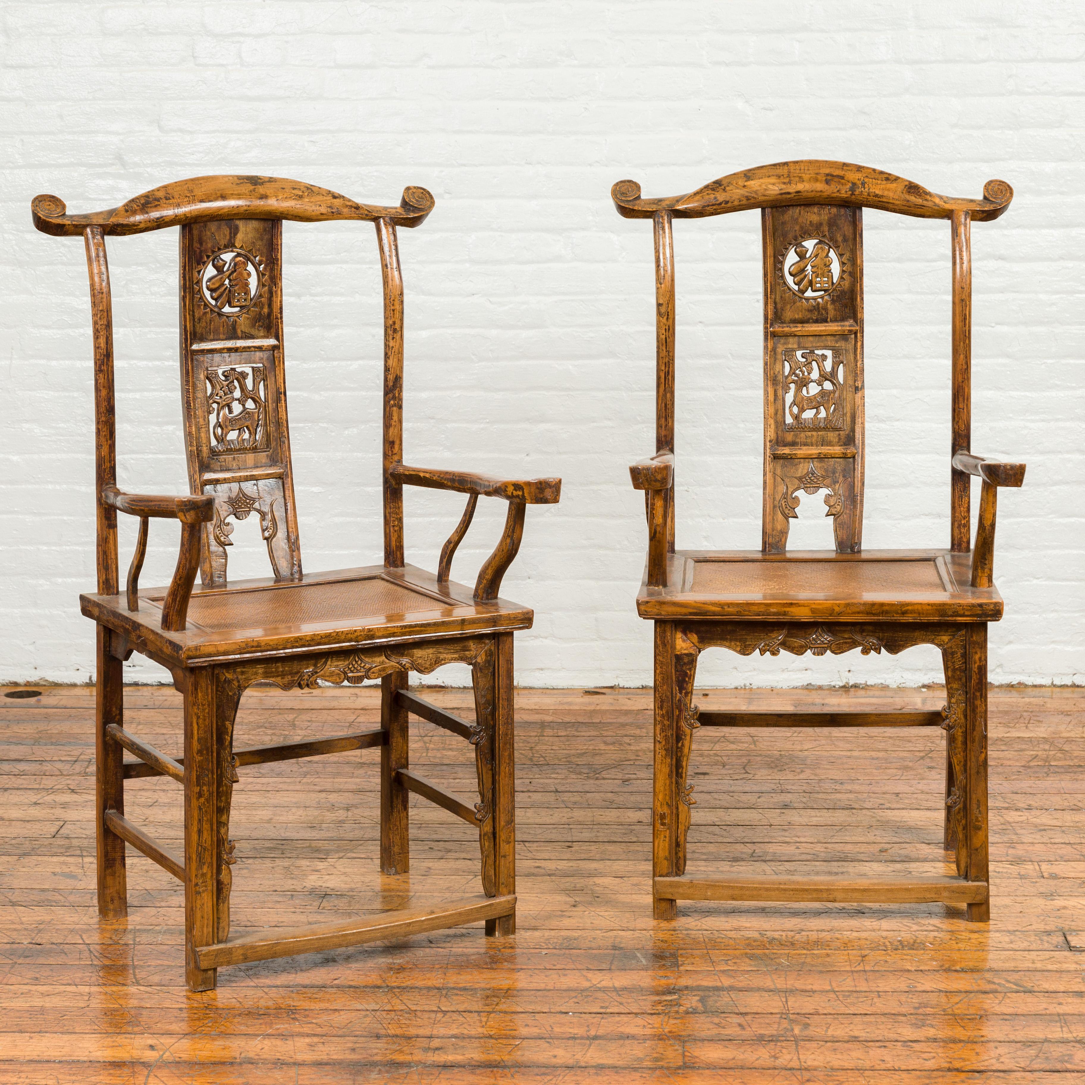 A pair of Chinese Qing Dynasty yoke back armchairs from the 19th century, with carved splats, brown patina, serpentine arms and side stretchers. Born in China during the Qing Dynasty, each of this pair of armchairs features a tall back, topped with