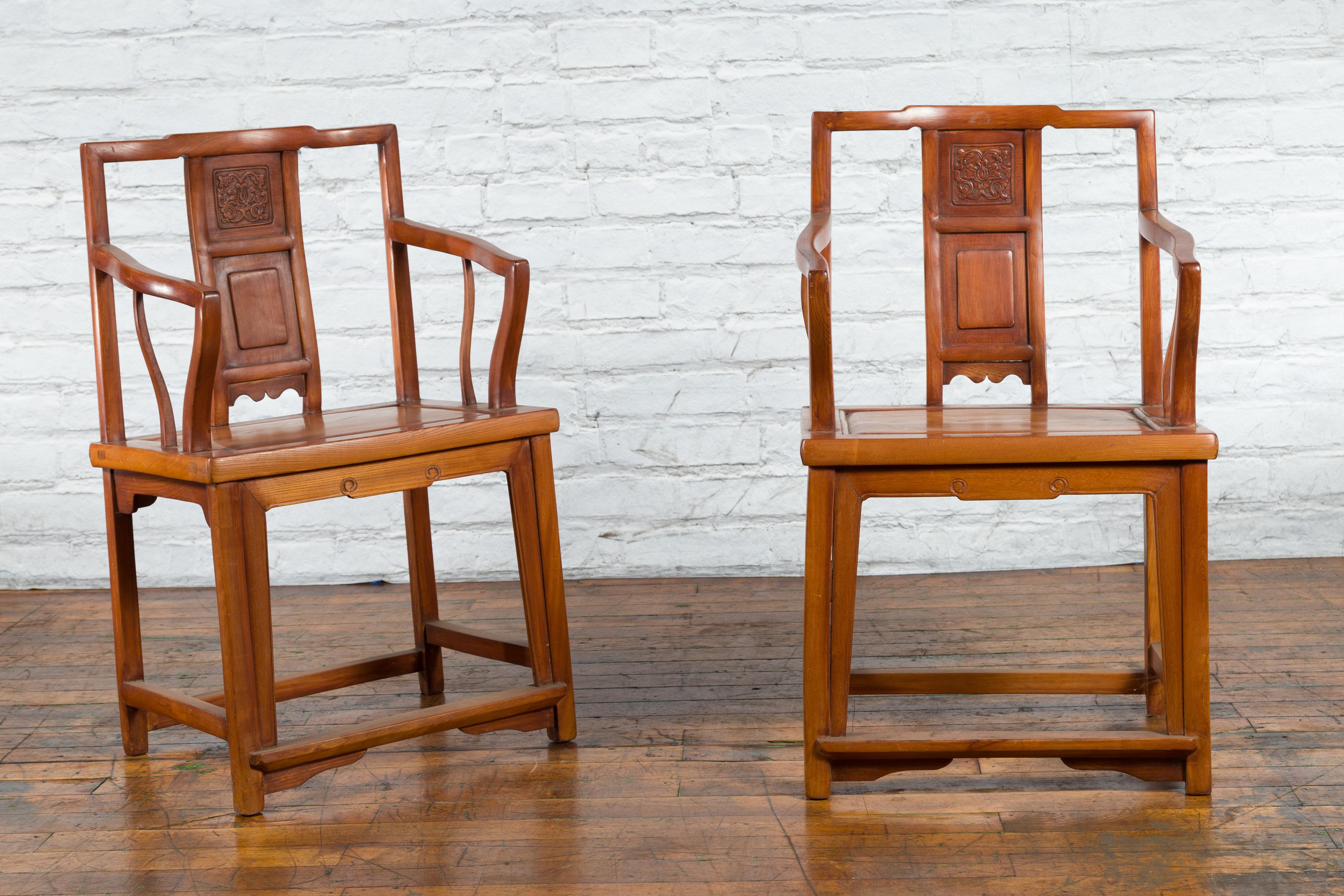 A pair of Chinese Qing Dynasty period lacquered elmwood armchairs from the 19th century, with carved splats, serpentine arms and stretchers. Created in China during the Qing Dynasty in the 19th century, each of this pair of elmwood armchairs