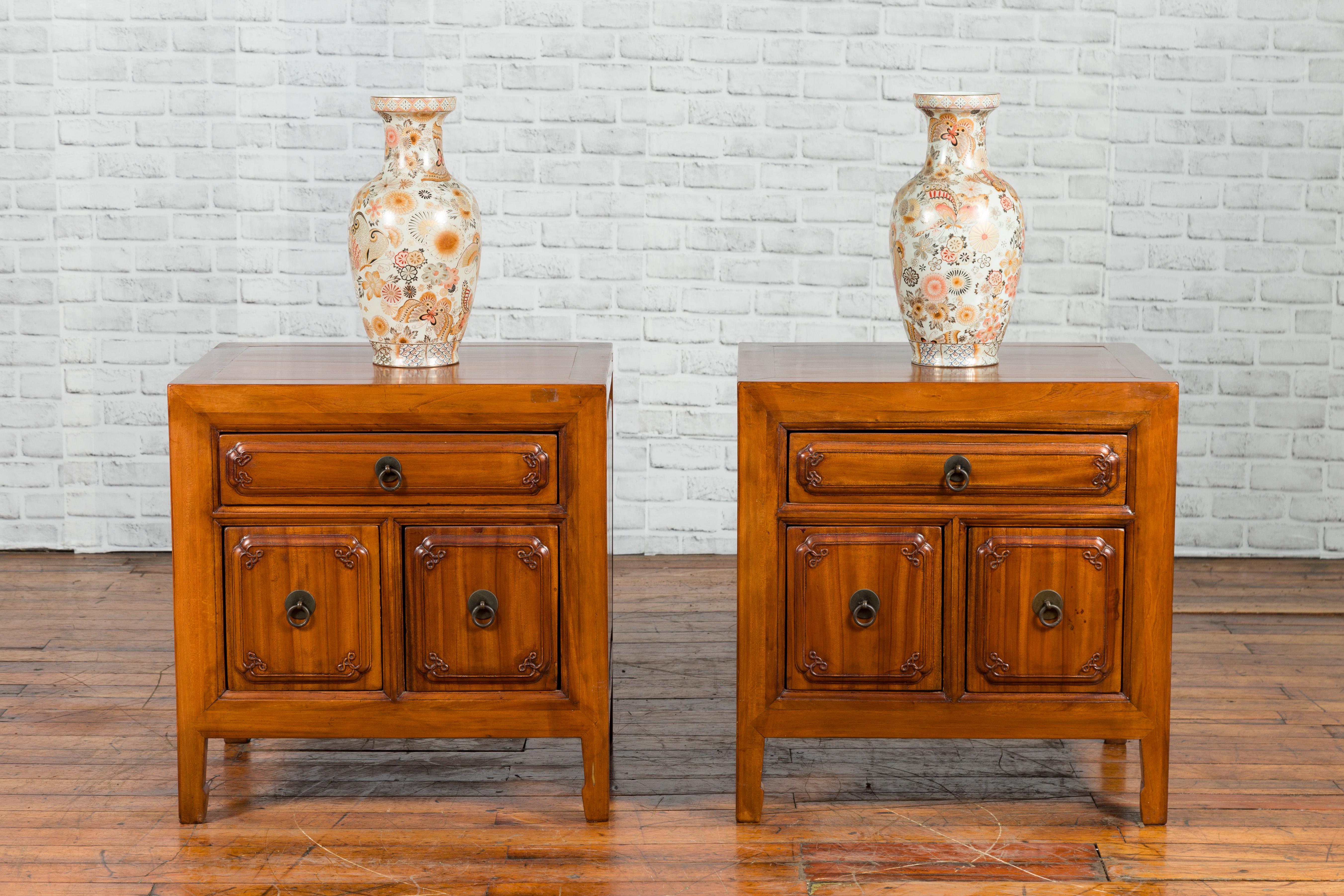 A pair of Chinese Qing dynasty period natural elm low cabinets from the 19th century, with three drawers and carved motifs. Created in China during the Qing dynasty, each of this pair of low cabinets features a square top sitting above a perfectly