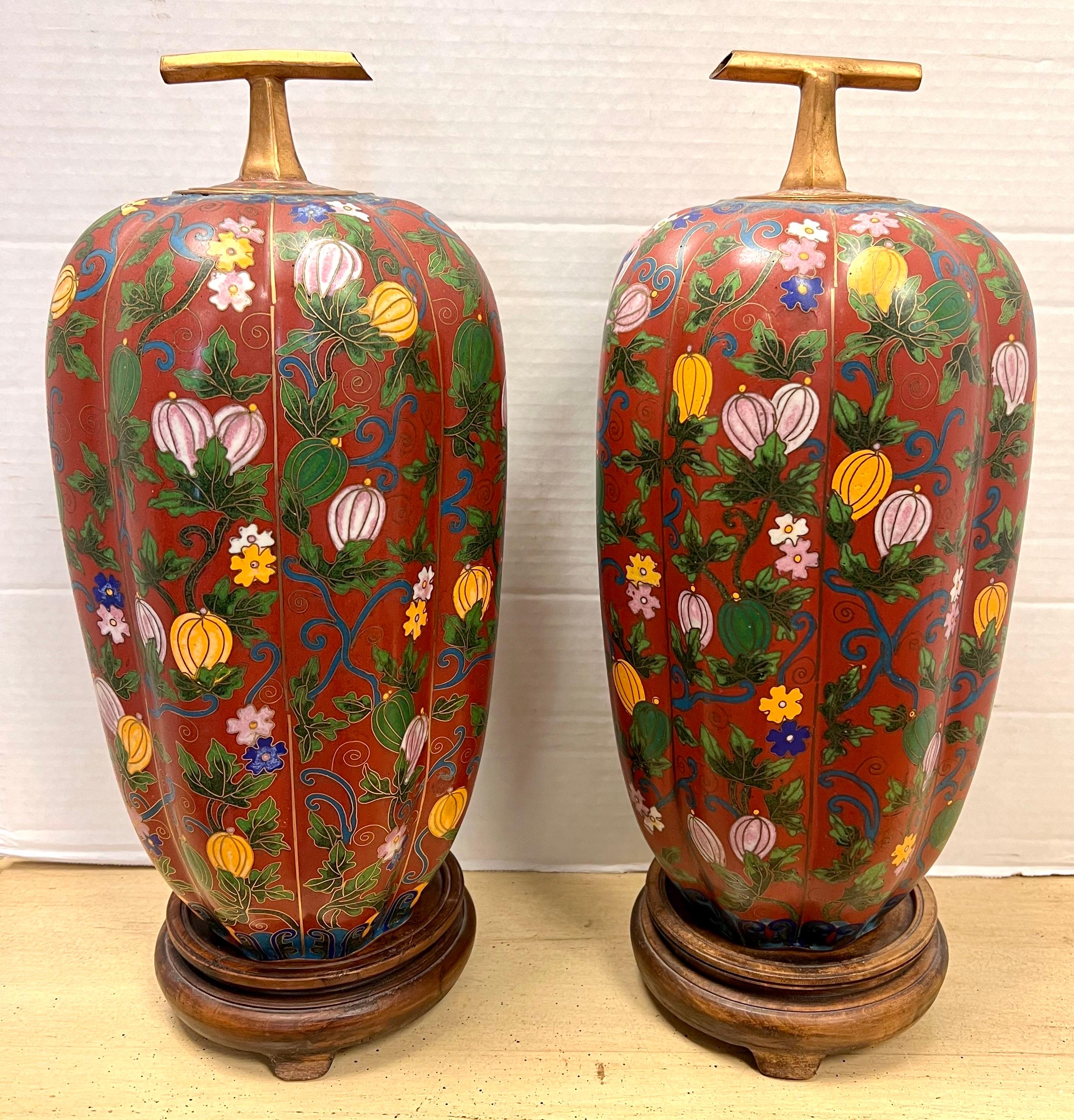 Rare pair of Chinese gilded covered vases with cloisonne enamel, decor of hand painted climbing ghords and flowers on a dark red background enhanced with gold tracery. Features bronze handles as stems. circa early 20th century. Note the wood bases