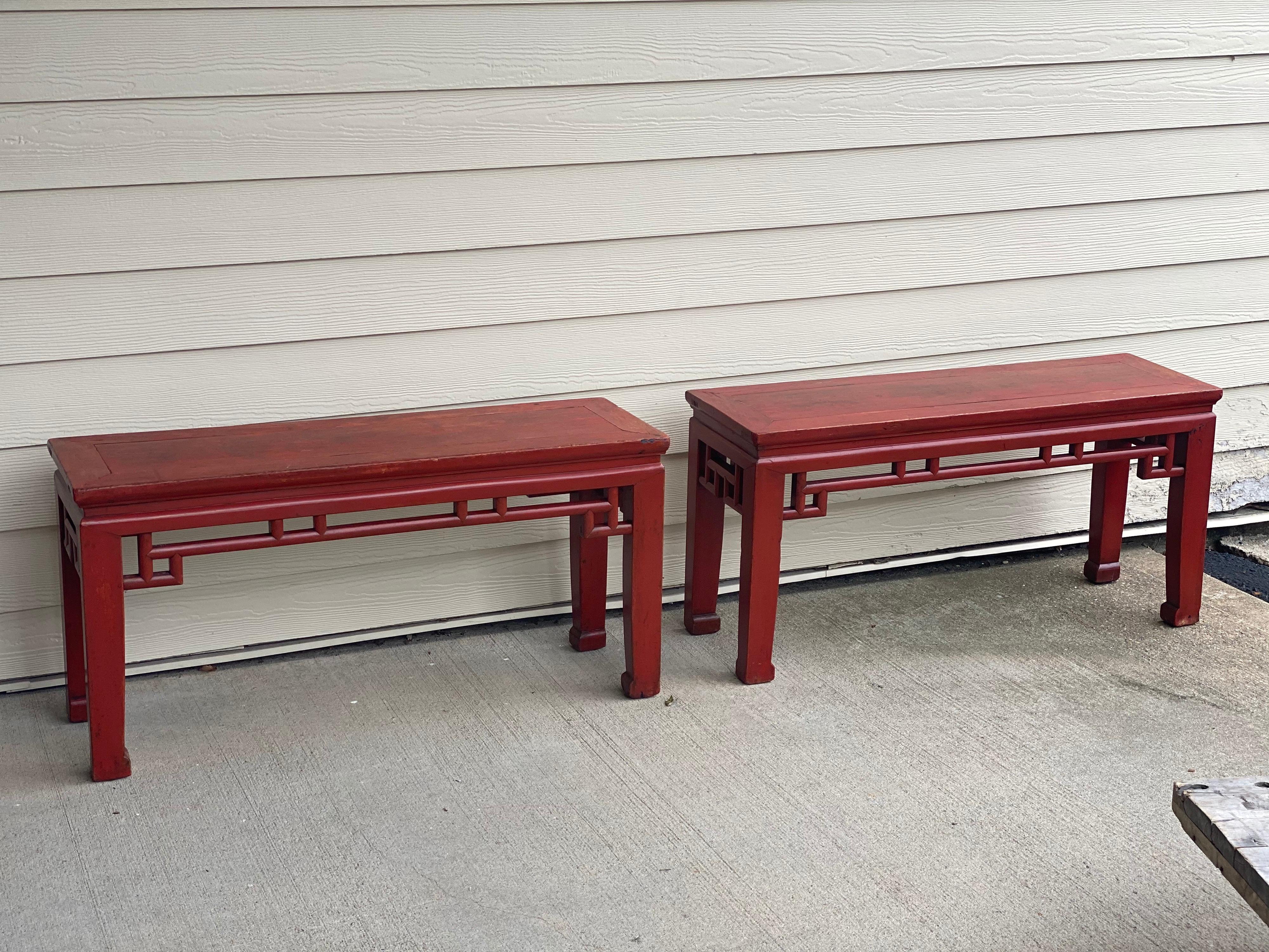 Pair of Chinese red lacquered low tables/benches
Lovely fret work on rail and sides. Classic Chinese Red Paint. Hoof feet. 
Expected wear to finish, mainly to the top.
Measures: 39.25