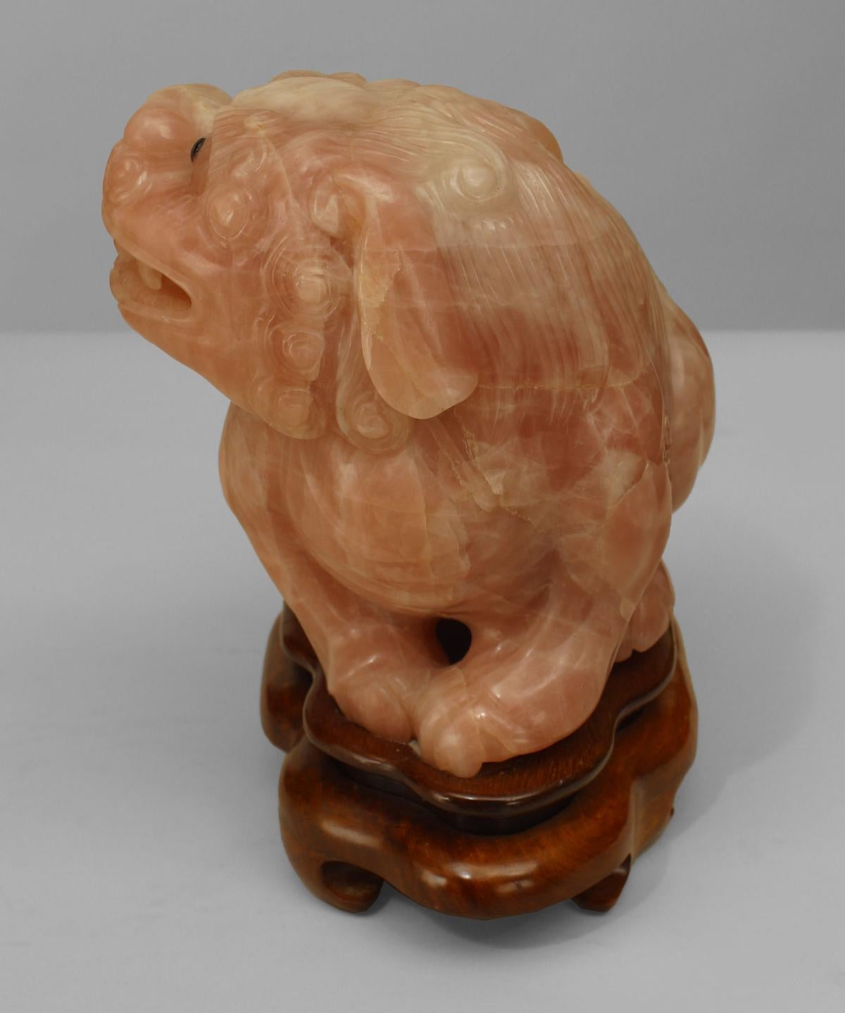 Pair of Asian Chinese rose quartz foo dogs with black eyes seated on teak bases (20th Cent).