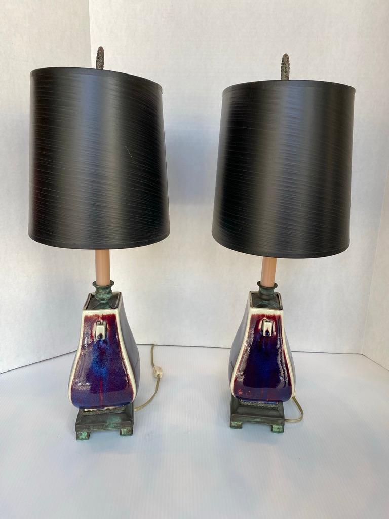 Pair of matching Chinese ceramic Sang de Boeuf lamps with black oval lampshades. Ceramic lamps having the traditional Chinese vase shaped body on metal bases, 1950s. Finials in the laurel wreath design. Lamp measures 4.5