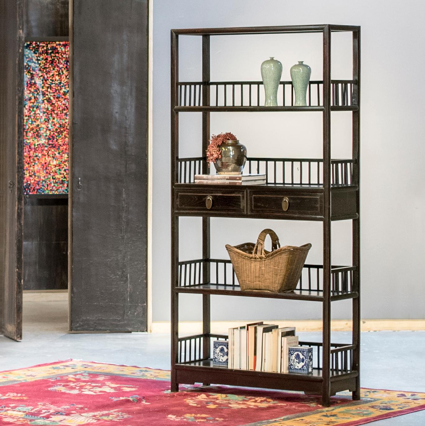 Dated to the early 20th century, these upright display shelves are constructed with lightweight frames, open sides, and low slatted railings enclosing each shelf. The pair's clean lines are accentuated by a dark brown-black finish, lightly faded at