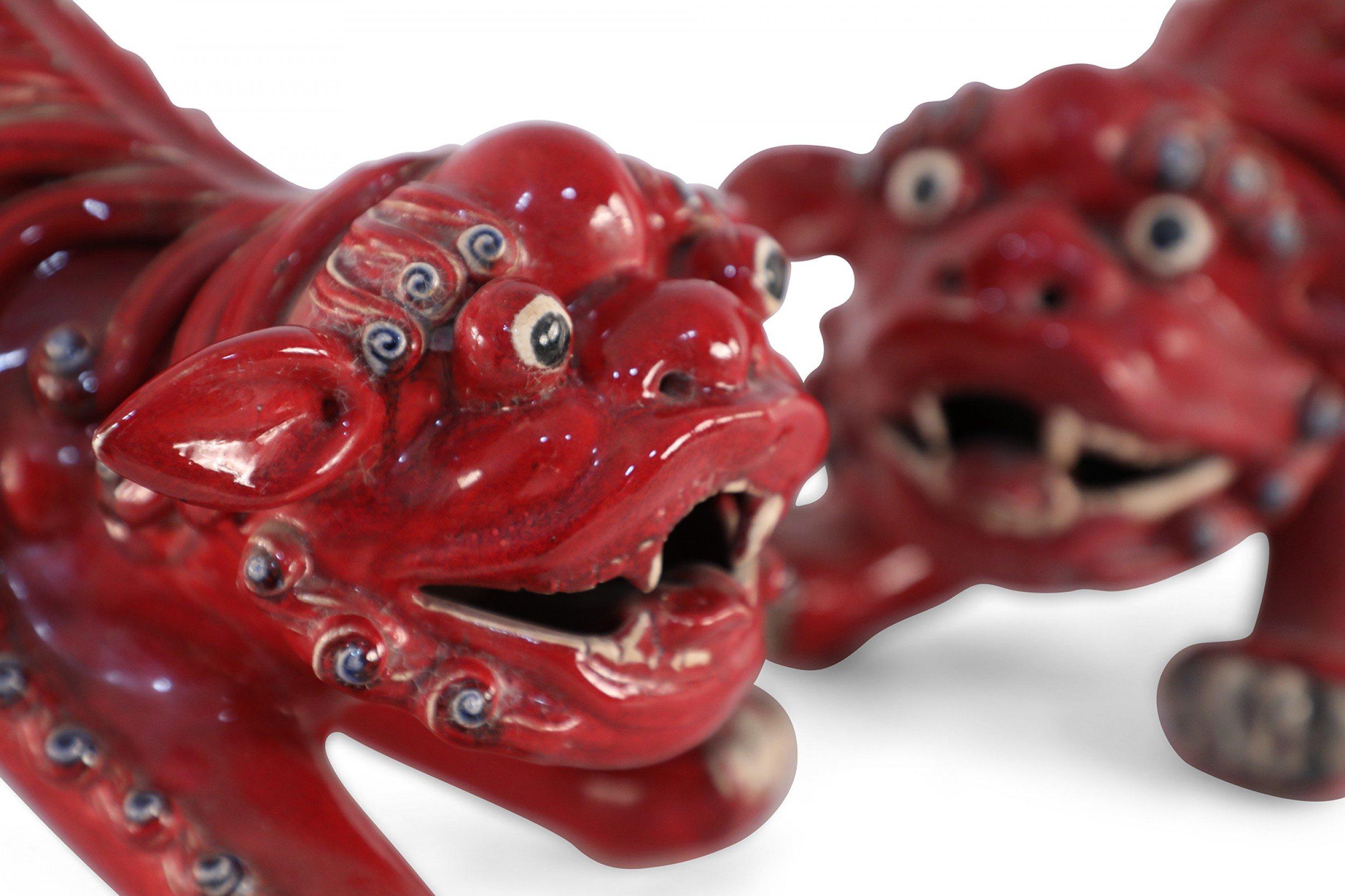 Pair of Chinese red porcelain foo dogs with spirited expressions, detailing, and shiwan town in guangdong forms- home to one of the most famous folk kilns during the ming and qing dynasties, renowned for their vivid animal models (priced as