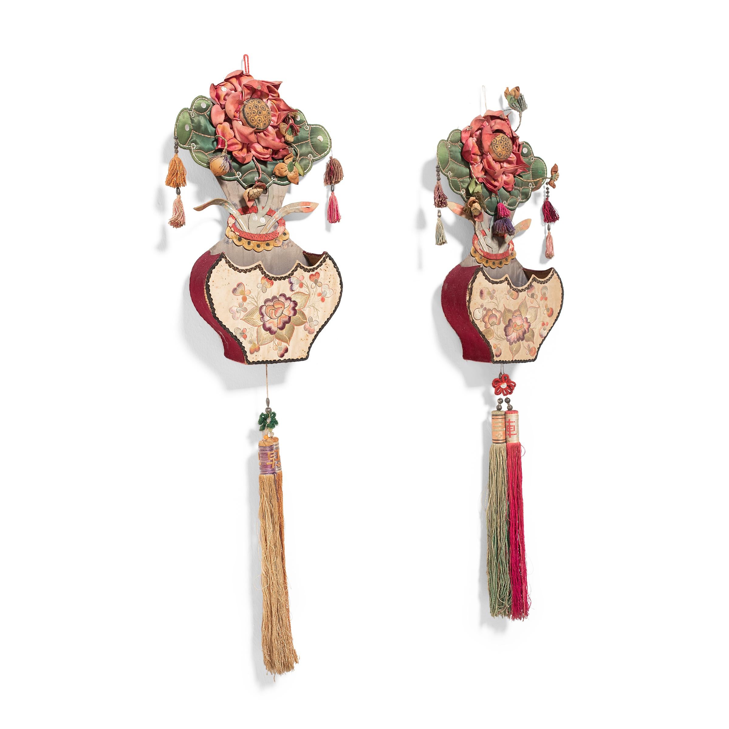 This pair of early 20th century wall pockets is crafted from colorful silks in the shape of two porcelain vases filled with lotus blossoms. Folds of pink silk comprise a large lotus flower atop each pocket, backed by a large lotus leaf of quilted