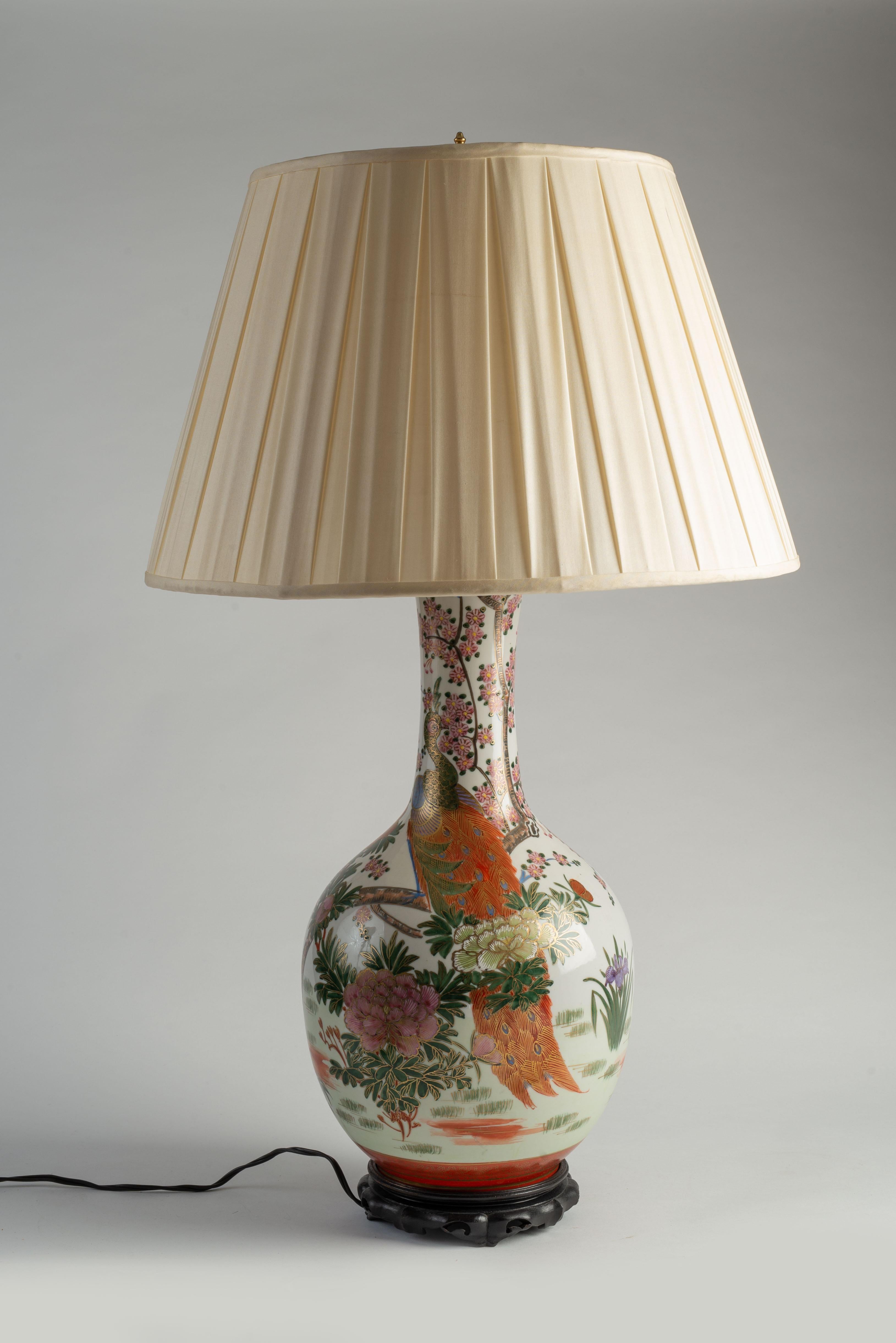 Each porcelain vase finely decorated with vividly colored flowers, reeds and peacocks in the Chinese Famille Rose style, each raised on a Chinese style wood base and adorned with a silk shade. 