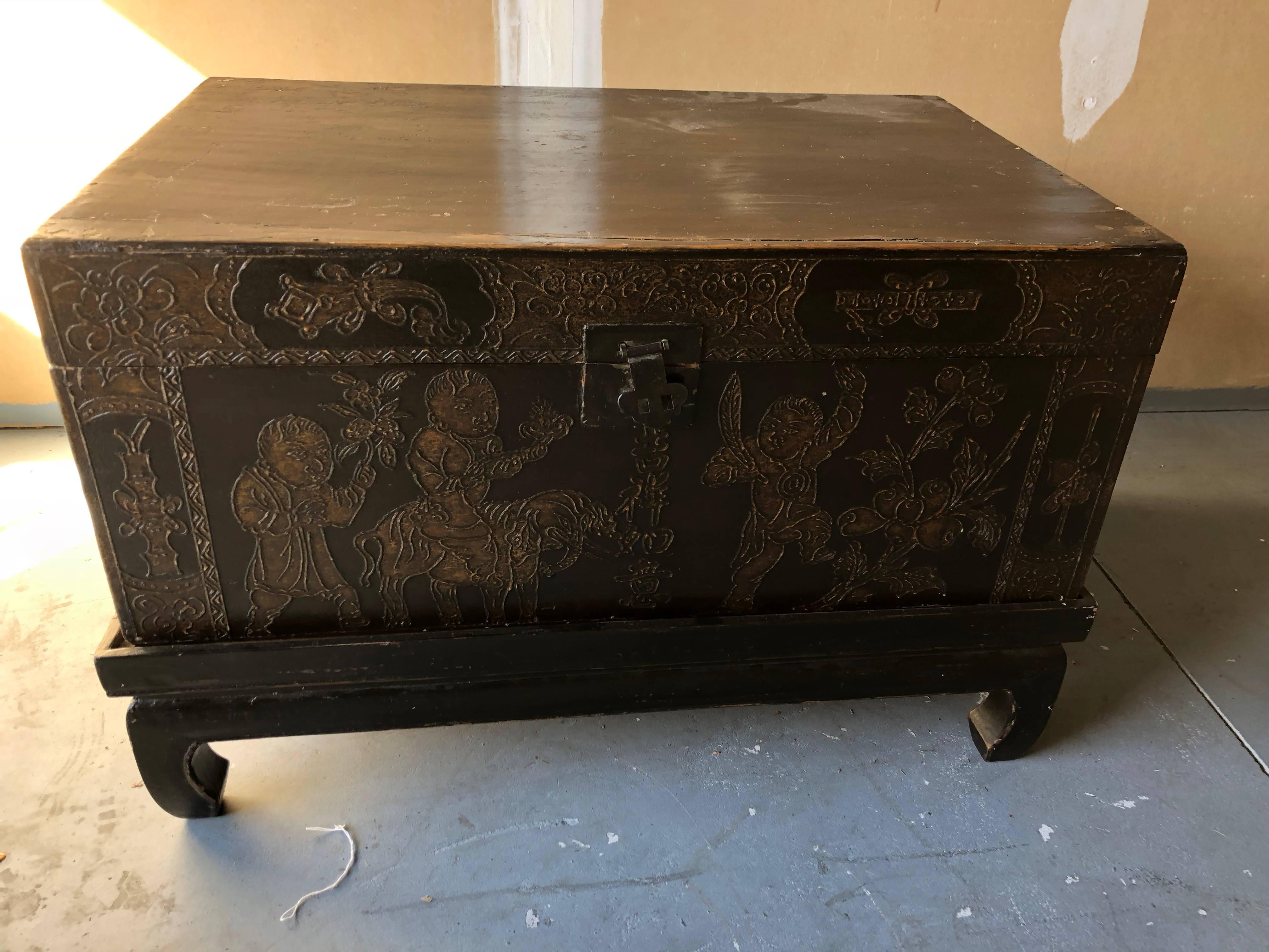 This pair of black lacquered trunks have handmade stands with hoof feet. Gold leaf hand painted fronts showing children at play. The locks and hinges are brass. Can be a coffee table or used as side tables.