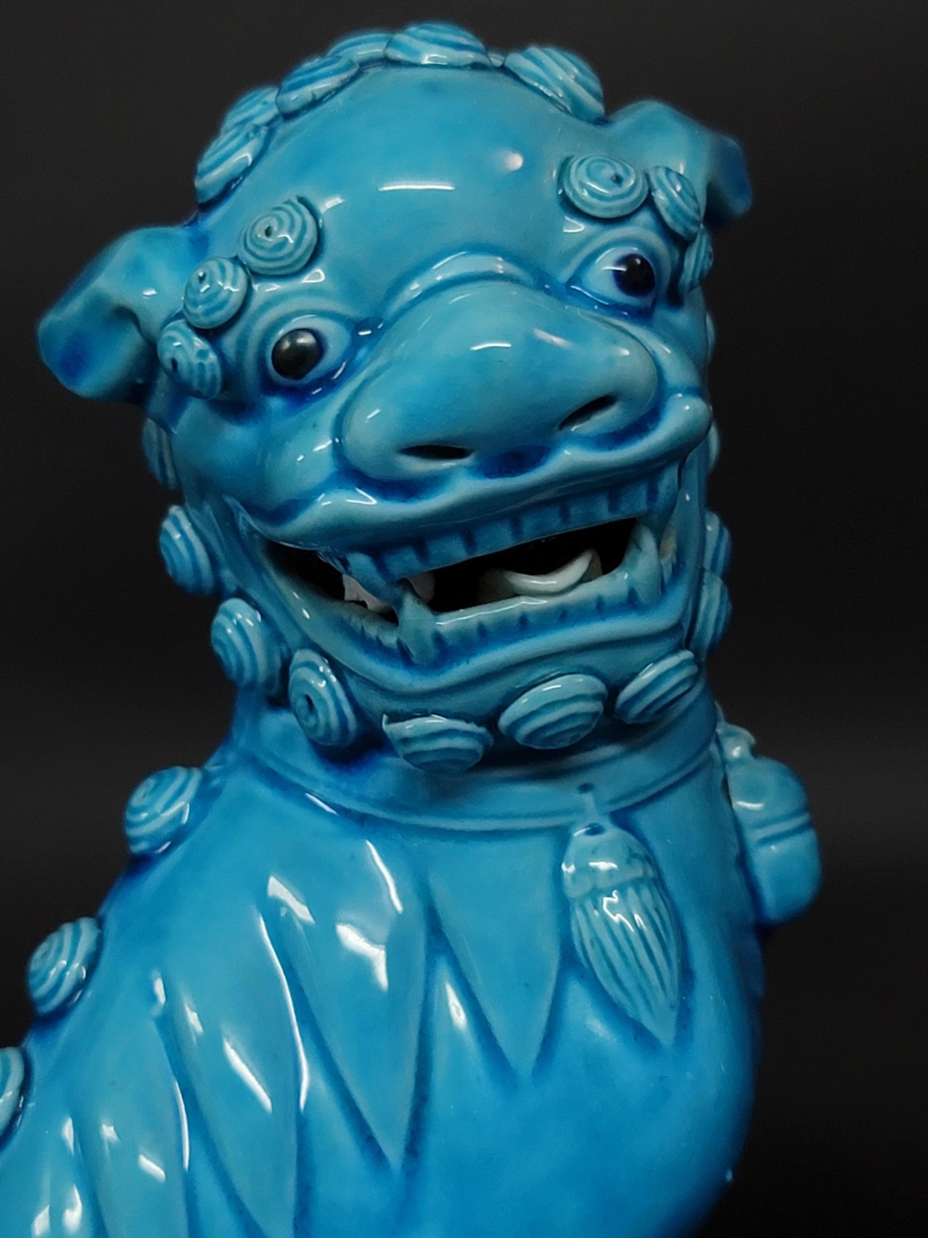Fine and very detailed pair of Chinese turquoise glazed foo dogs from the mid 20th century. The hollow biscuit porcelain figures stand raised on a rectangular base and are looking sideways with open mouths and tongues showing teeth each with a