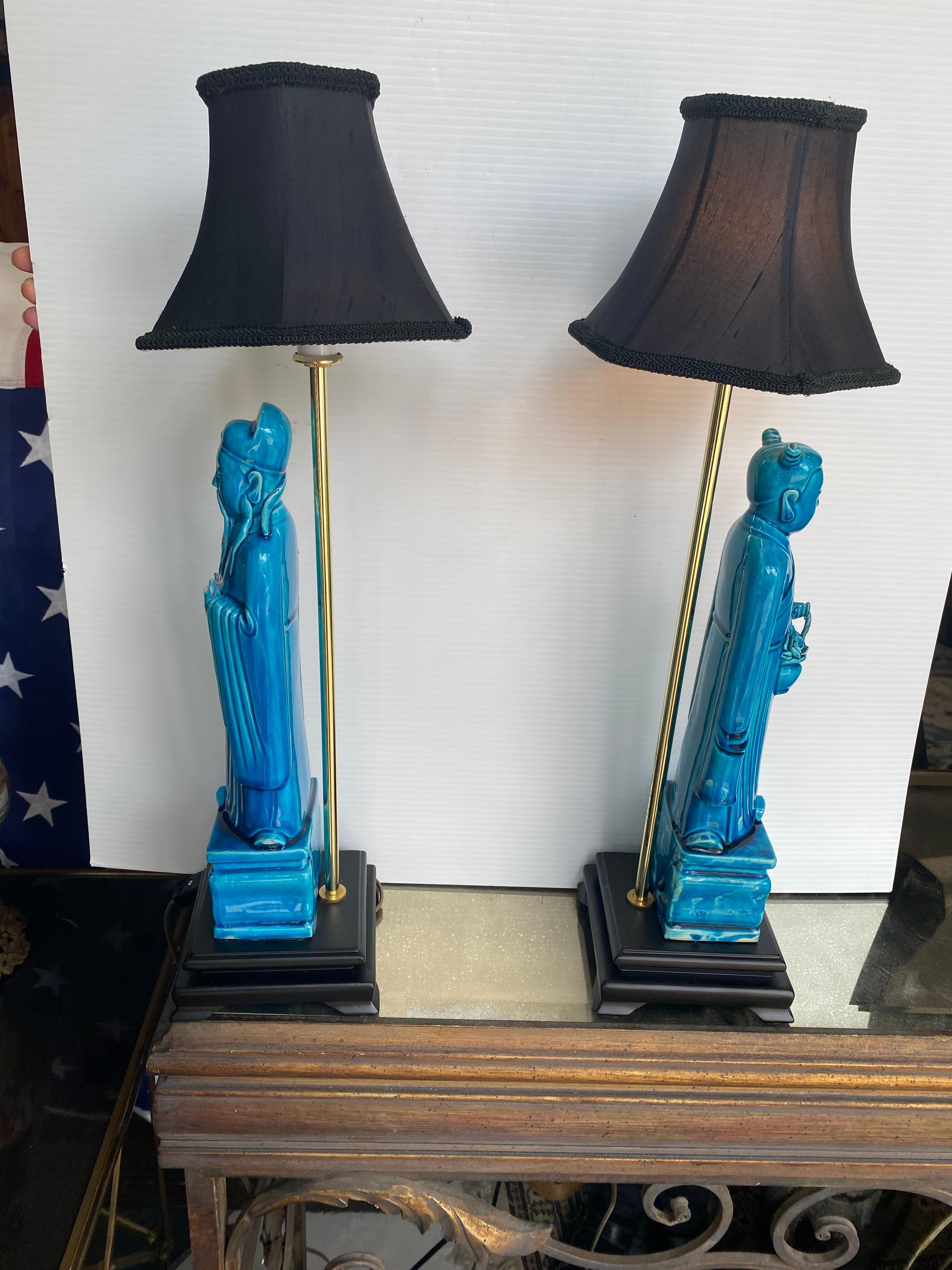 A pair of dark turquoise small lamps having a male and female standing under the shade standing on a black base newly wired.