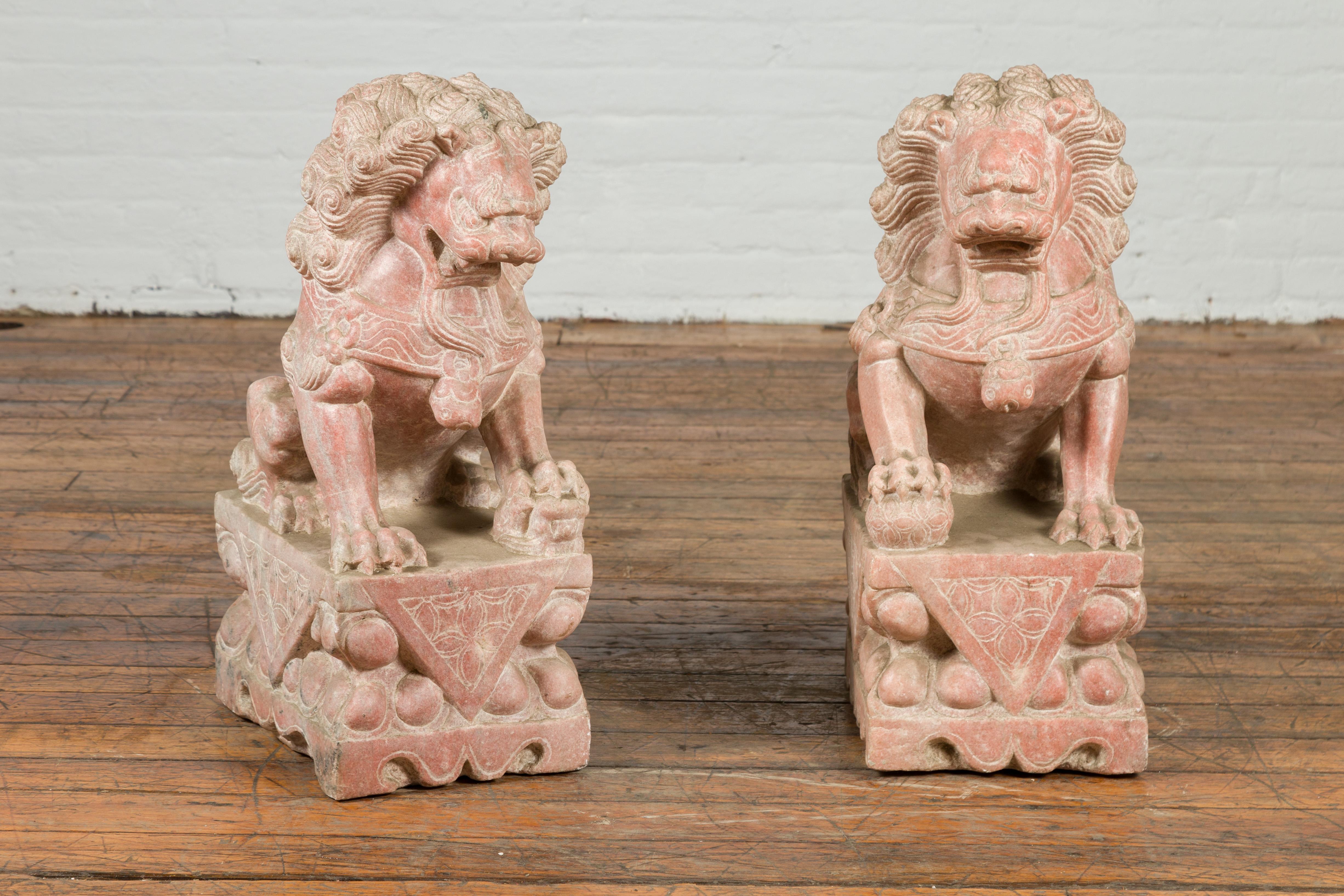 A pair of vintage Chinese stone Foo Dogs guardian lions from the mid-20th century, with sandstone patina, on rectangular bases. Created in China during the midcentury period, this pair of Chinese guardian lions features a left and right facing male