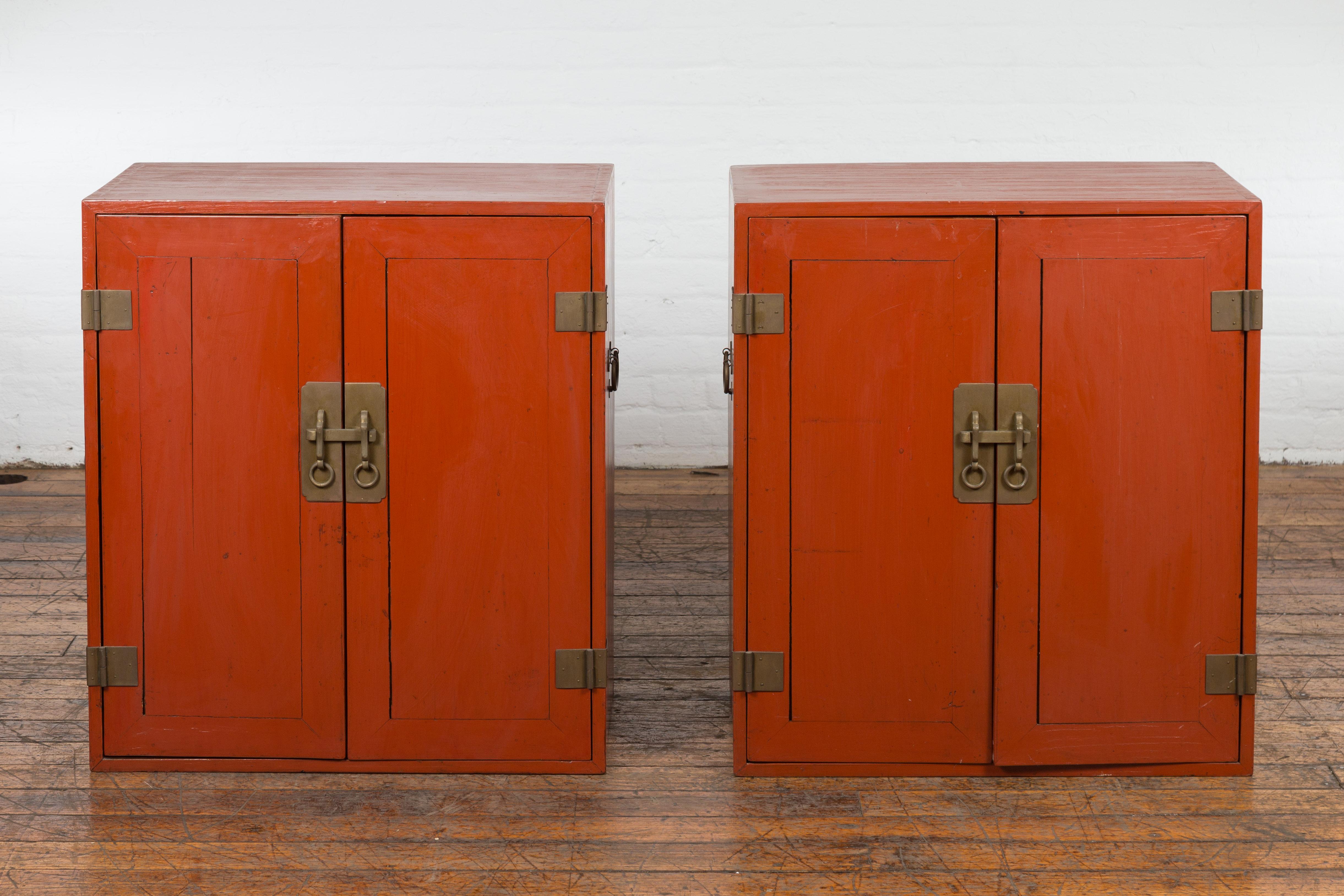 A pair of vintage Chinese side cabinets from the Mid-20th Century, with red lacquer finish, pairs of double doors, four interior boxes each and traditional brass hardware. Created in China during the mid 20th century, this pair of side cabinets