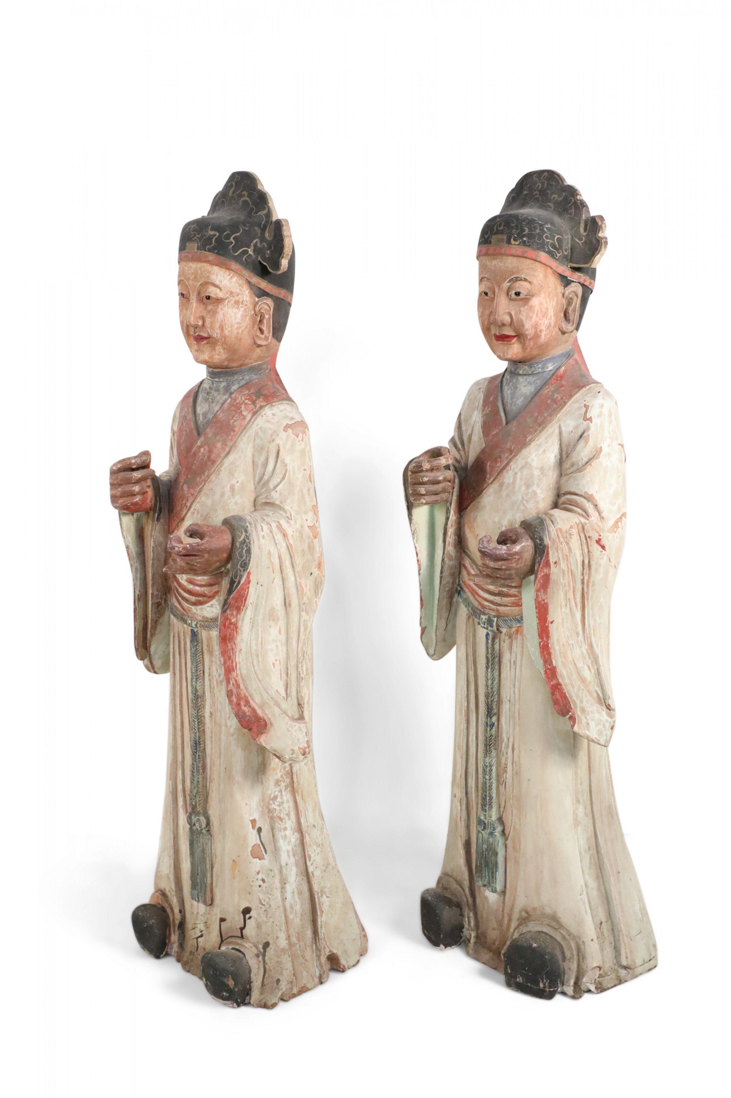 2 chinesische geschnitzte Holzstatuen von Beamten in weißem Gewand mit roter Verzierung und einem Quastengürtel an der Taille (Preis pro Stück).
 