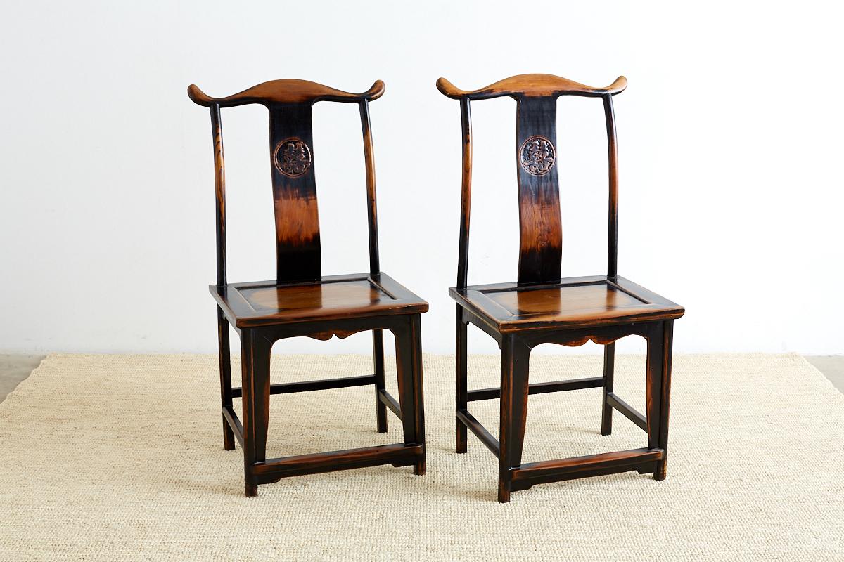 Dramatic pair of Chinese yoke back official's hat chairs featuring a Shuangxi emblem on the backsplat. These carved chairs have a lacquer finish with a distressed worn look and craquelure patina. Beautifully made with old world joinery and a smooth