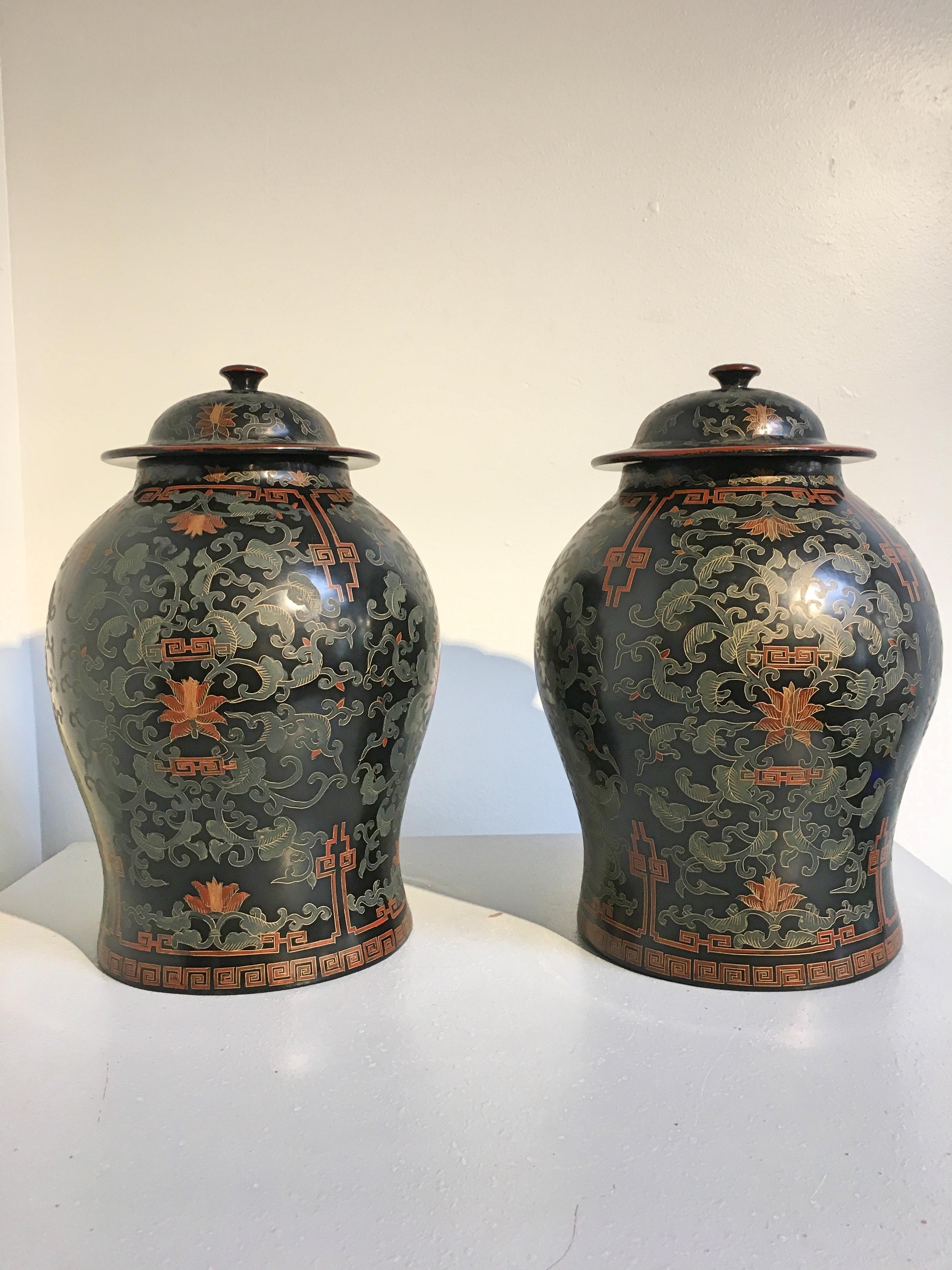 A handsome pair of chinoiserie painted and black lacquered wooden temple jars, circa 1980s. 

The wooden jars of baluster form and surmounted by a domed lid. The jars painted in red and green pigments with a floral and foliate design of stylized