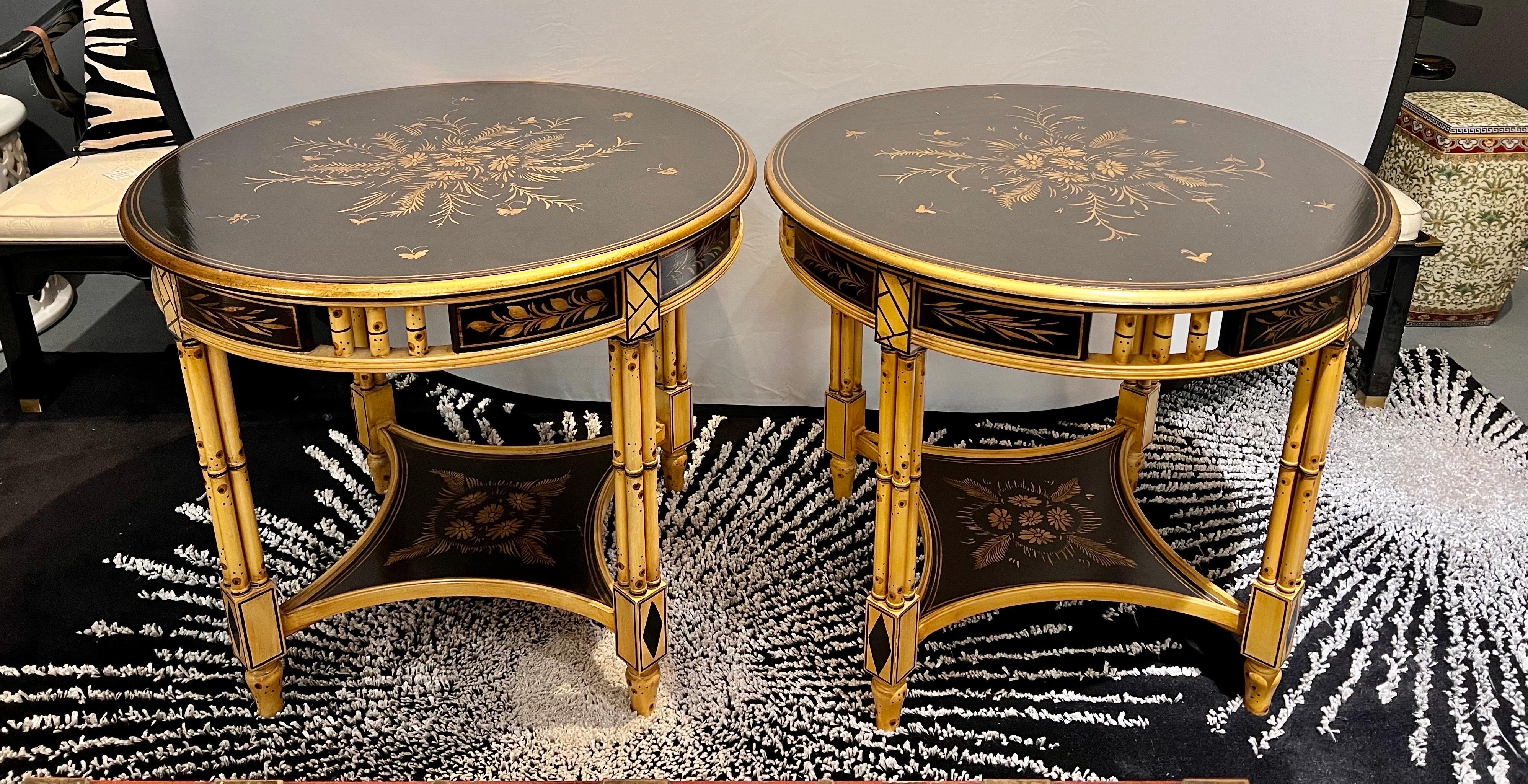 Pair of two beautiful chinoiserie style black lacquered and faux bamboo two tiered side tables with hand painted gold painted floral motif on top and bottom shelf.