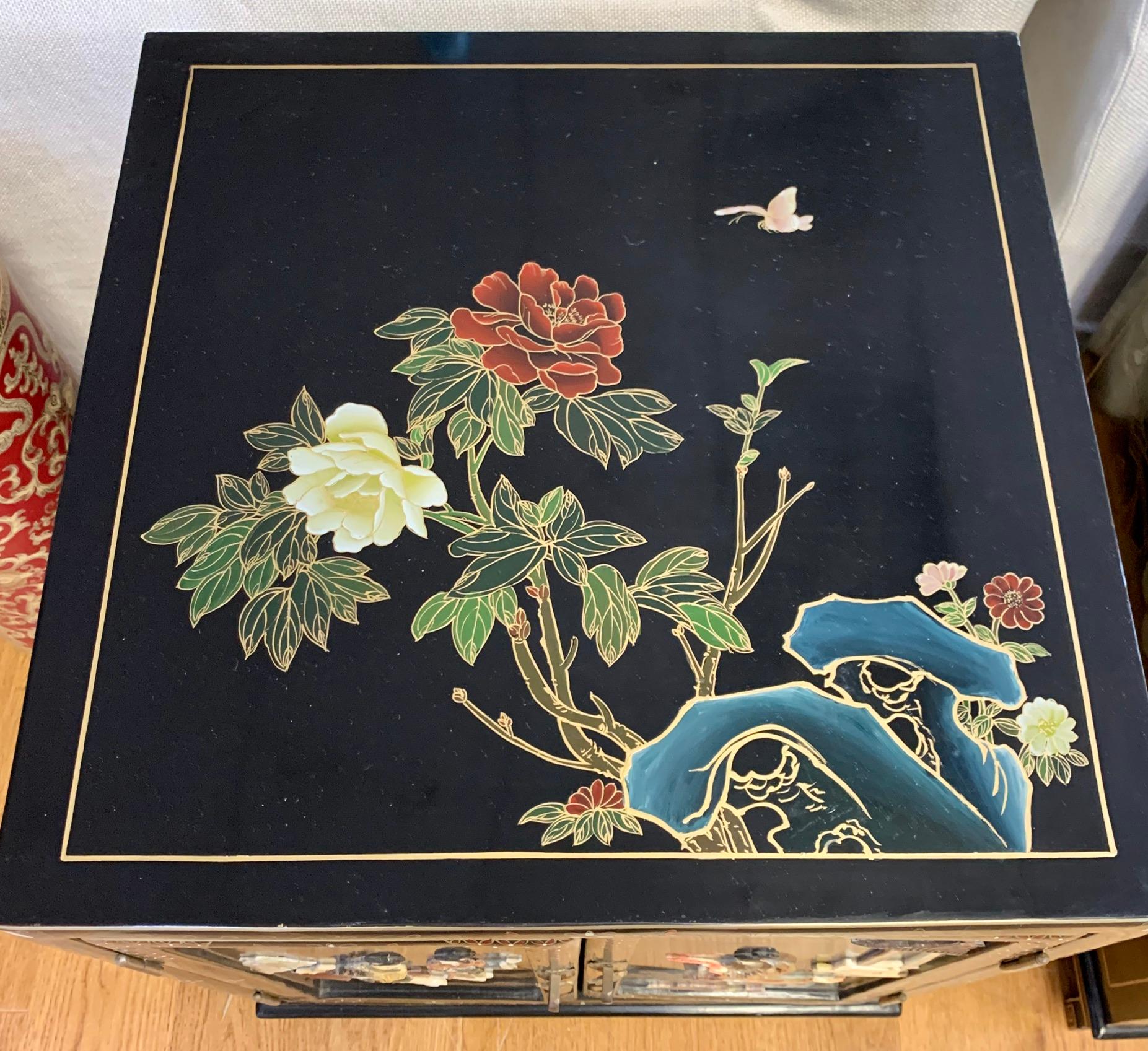 Elegant pair of chinoiserie black and gold lacquered chests/cabinets/end table or nightstands. Features carved hardstone figures on front doors and hand painted flowers and details throughout. Fitted glass on top. Gorgeous lines and better scale.
