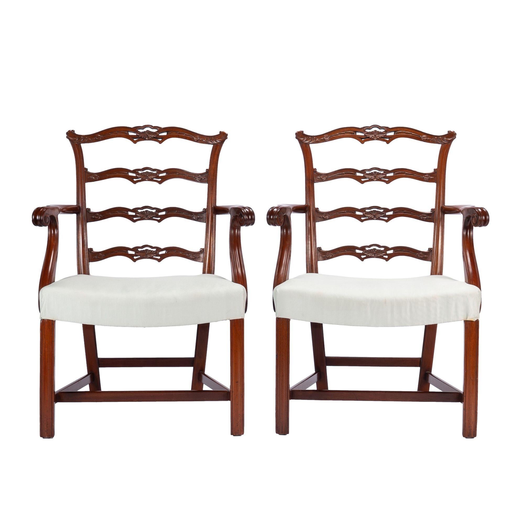 Pair of Academic Revival Chippendale solid mahogany arm chairs with exceptional pierced and carved ladder back rails. The over rail upholstered saddle seat is supported by molding carved square legs which are joined by an “H” stretcher. The shaped
