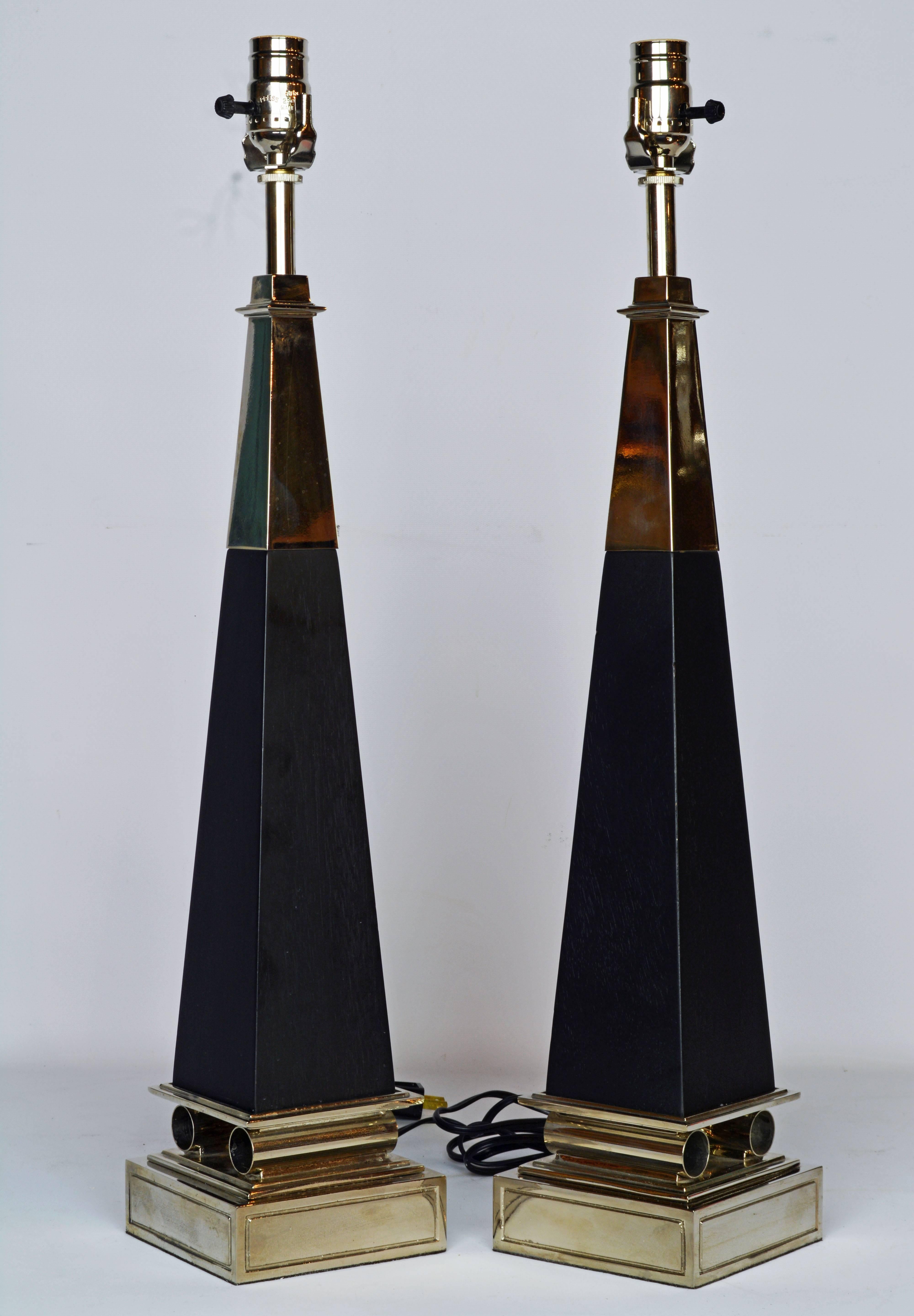 These Mid-Century Modern table lamps in the shape of obelisks represent an iconic Tommi Parzinger design. They feature chrome top sections above ebonized wood columns resting on a square chrome base intersected by classical inspired chrome cylinders.