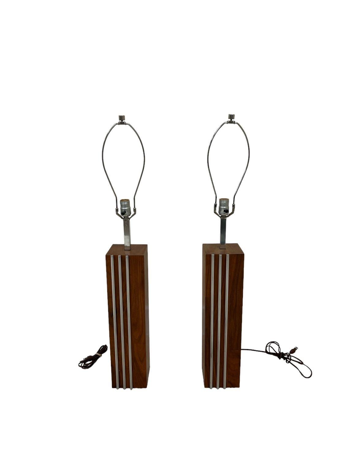 Pair of skillfully crafted simple walnut and chrome lamps by Laurel Lamp Company. Beautiful illustration of Mid Century lighting. Excellent craftsmanship of walnut veneer with three protruding aluminum bands. Marked Laurel lamp on the socket. Shades